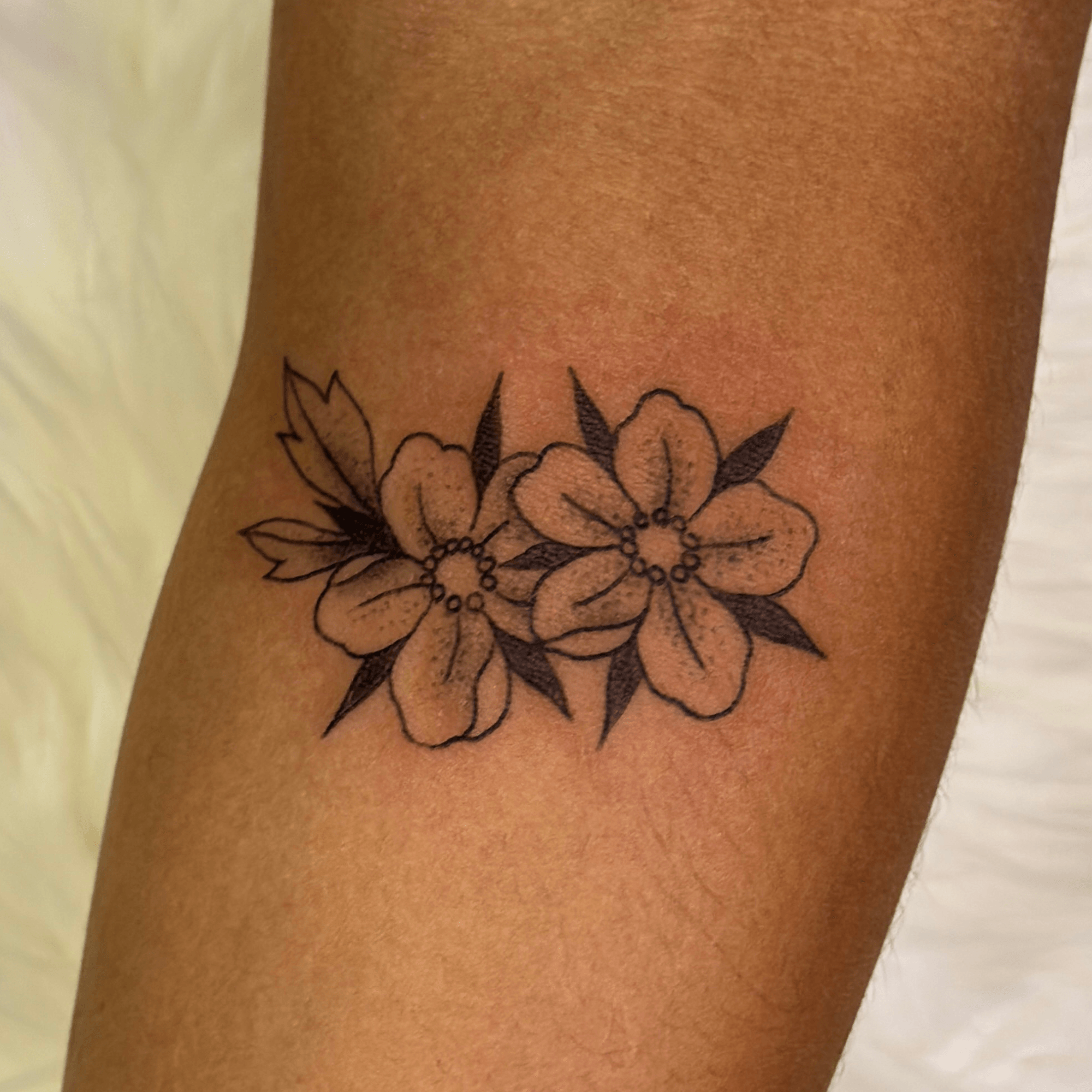 Black outline tattoo of two flowers with leaves on skin.