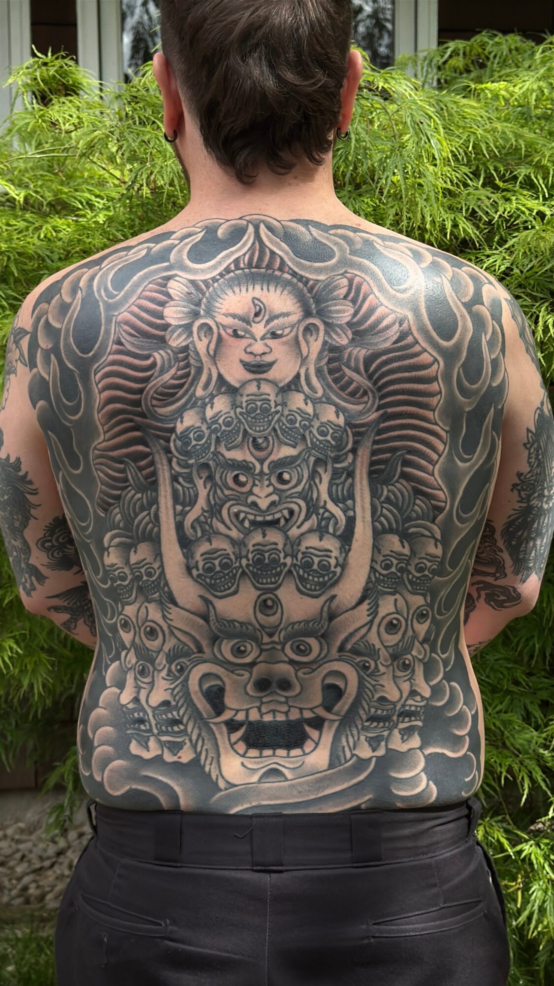 Back view of a person with an intricate black and gray tattoo covering the entire back, featuring a lion, tiger, and mythical creature.