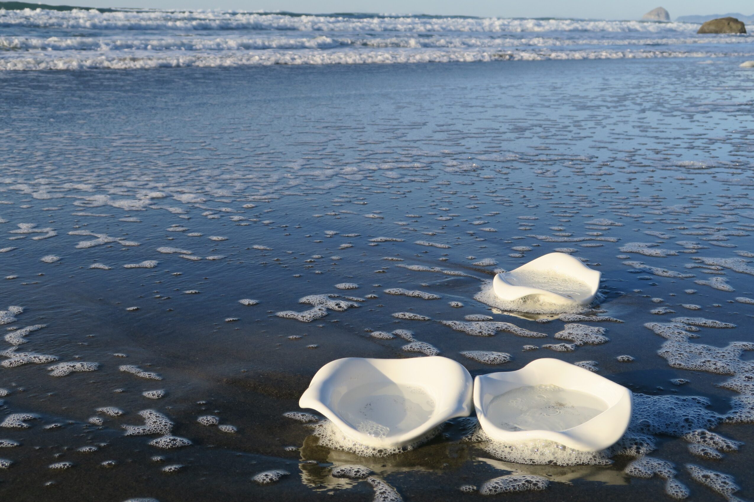 Three ice chunks floating on the ocean surface with waves and a distant shoreline in the background.