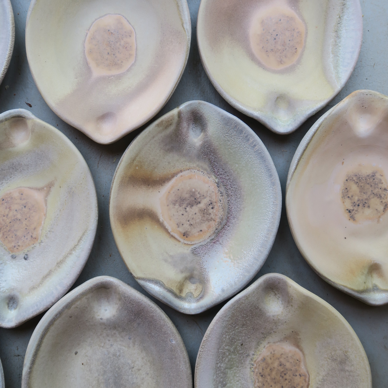 Close-up of multiple ceramic bowls with glazed, iridescent surfaces in various shades of cream, gray, and purple.