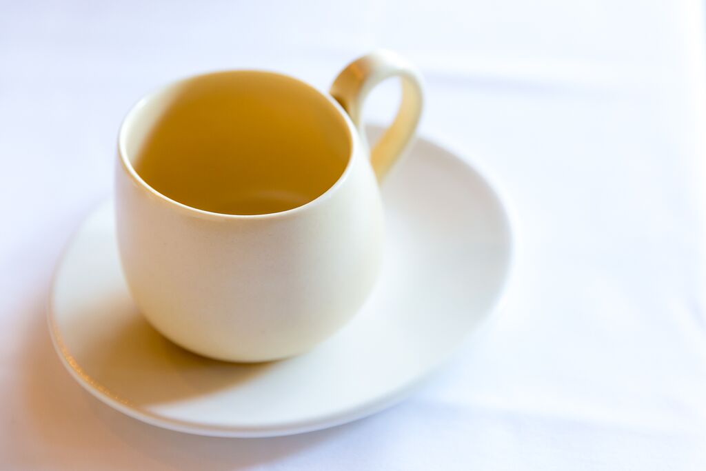 White cup filled with tea on a white saucer, placed on a white surface.