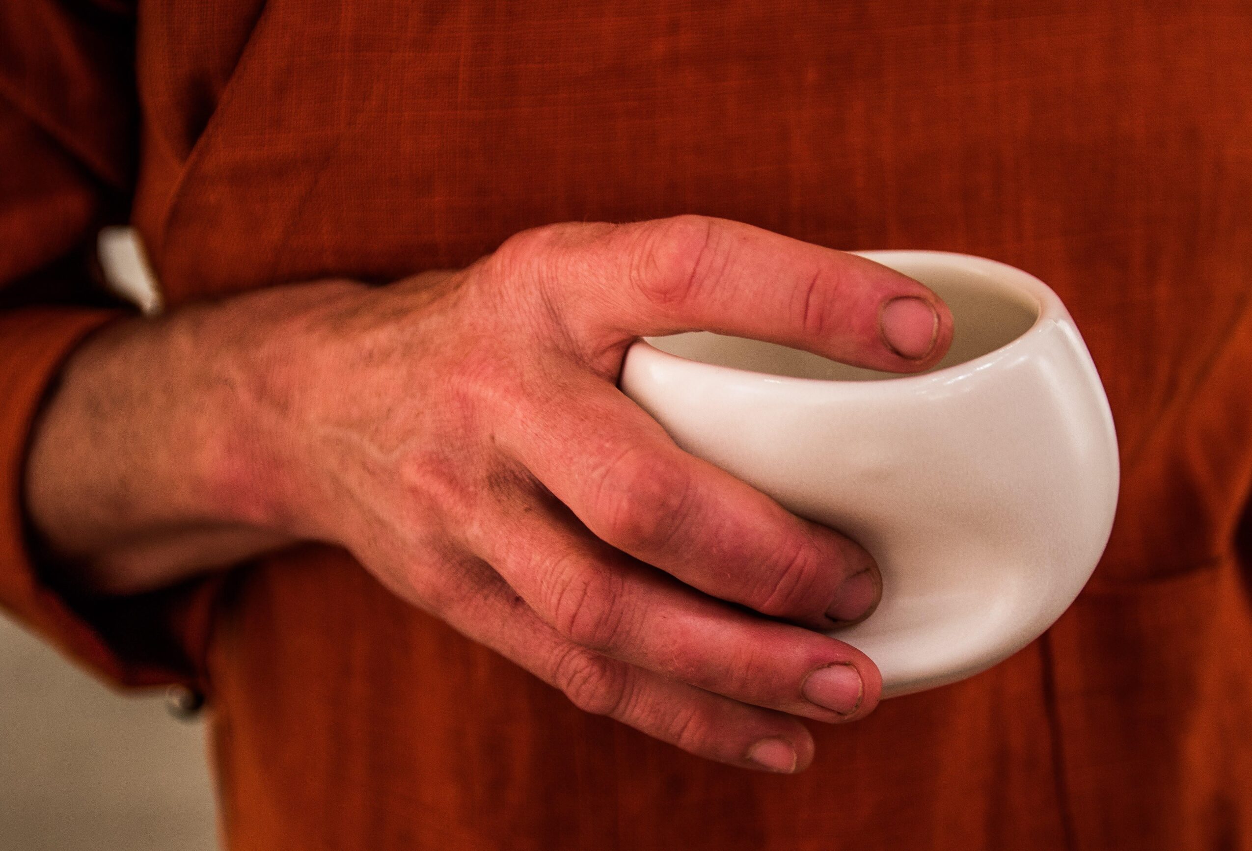 Person holding a white ceramic mug with both hands, wearing an orange-brown shirt or apron.