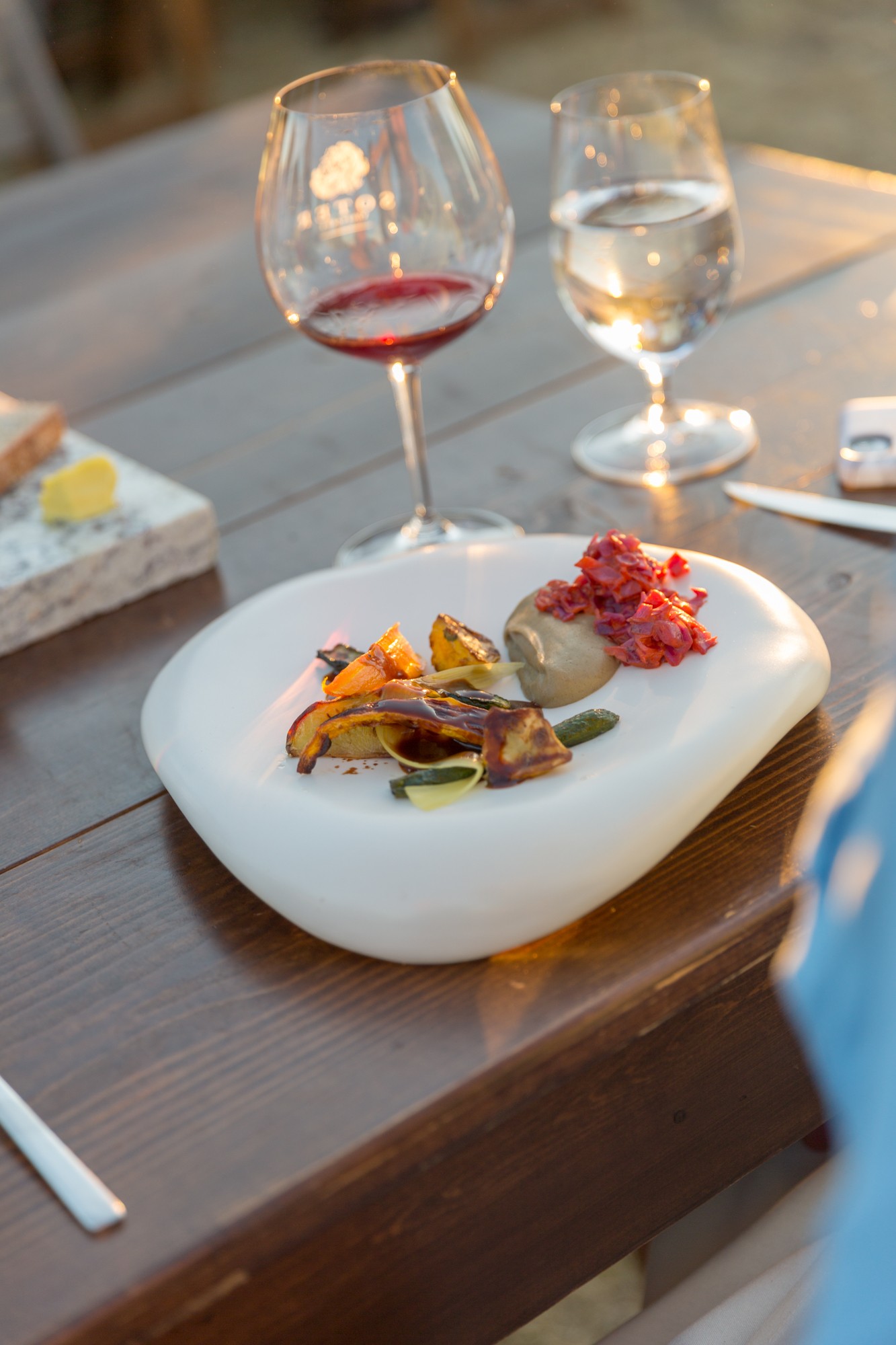 Plate with food, two glasses of wine and water on a table, outdoor setting, soft lighting.