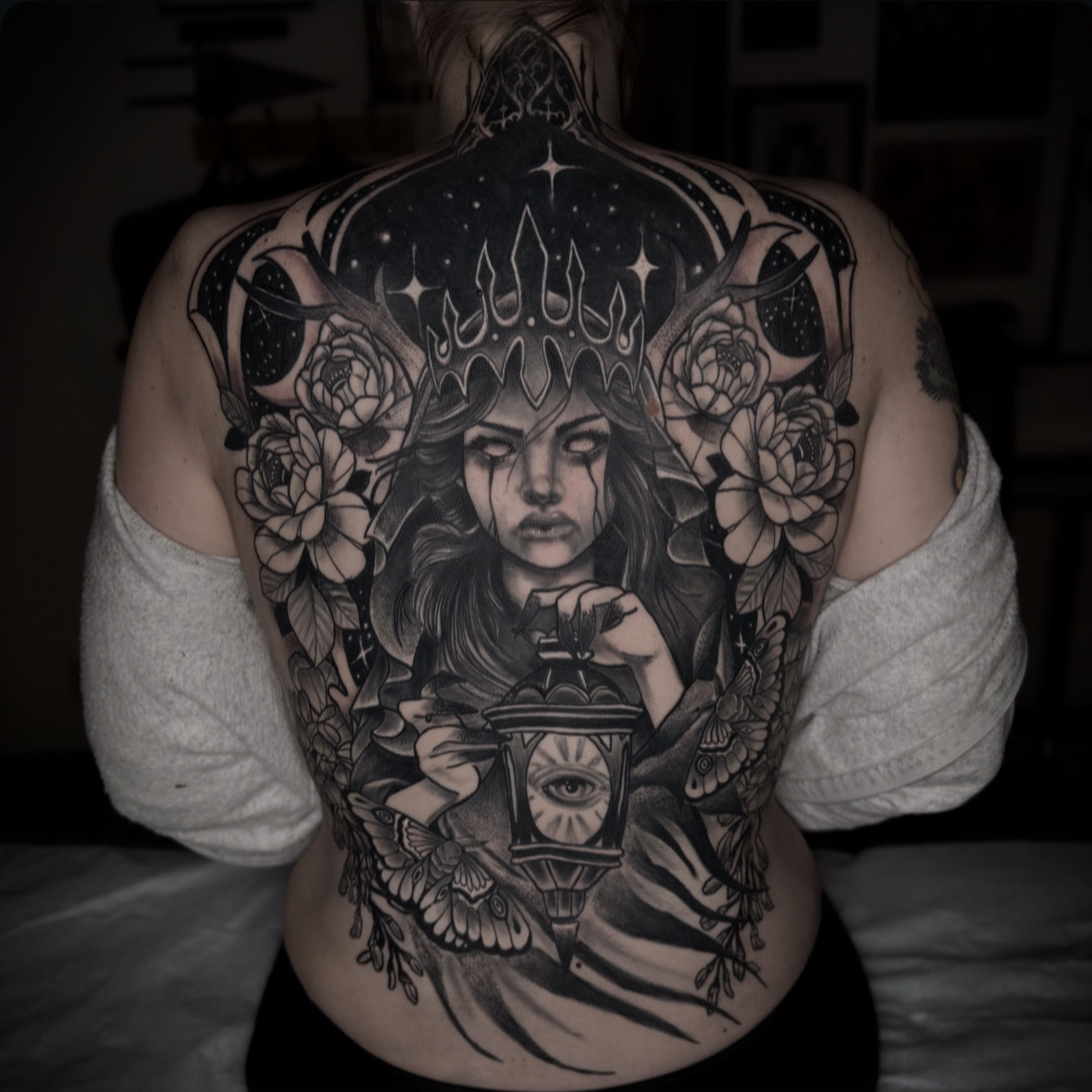 Intricate black and gray tattoo covering back, featuring a woman's face, flowers, and celestial elements.