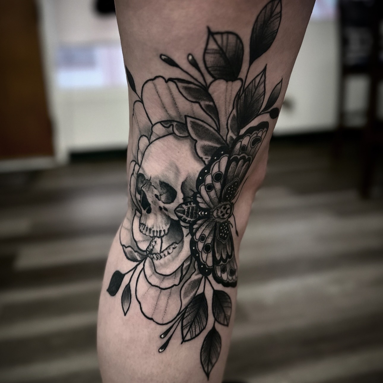 Black and gray tattoo of a skull, butterfly, and floral elements on a person's leg.