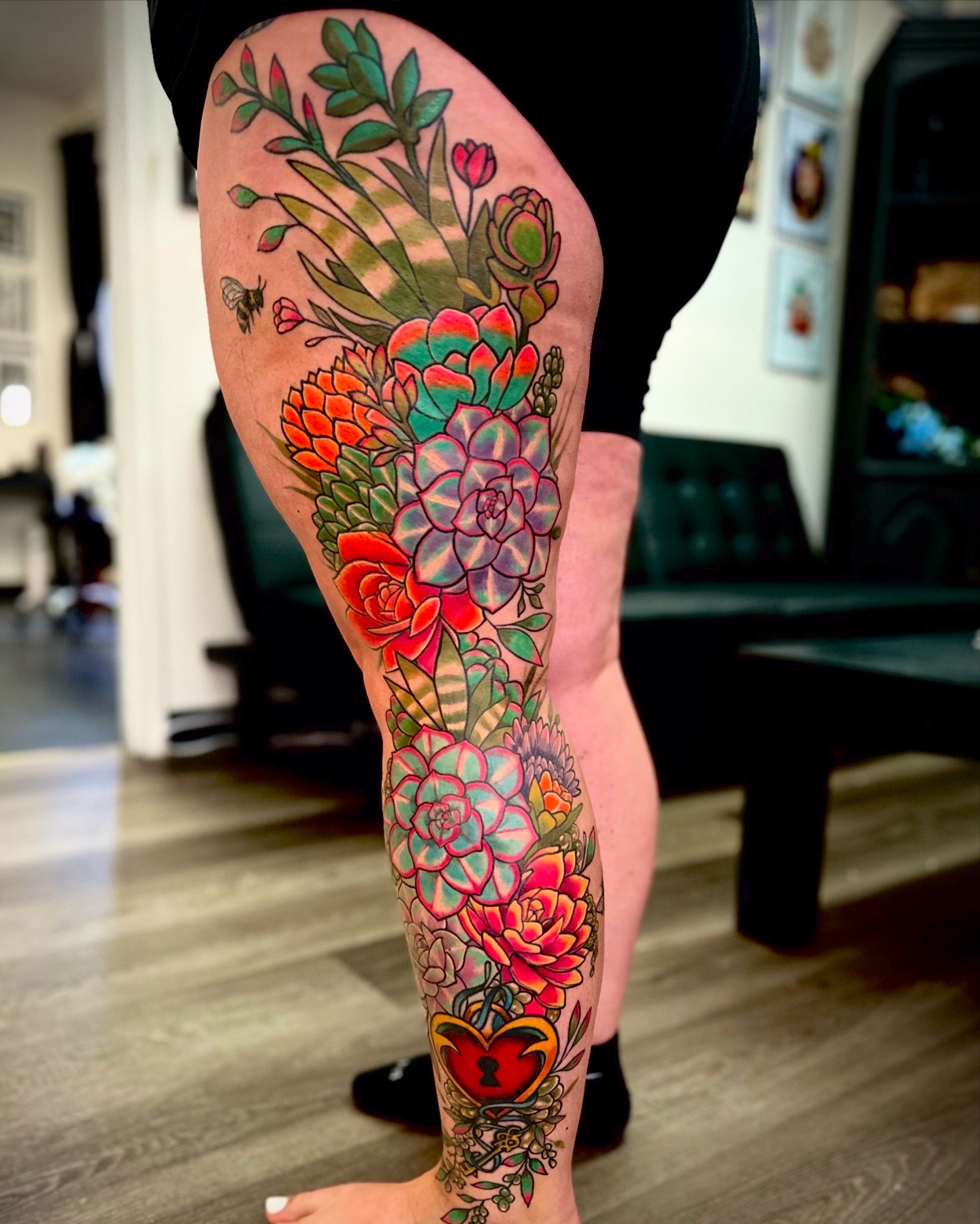 Colorful floral tattoo on person's leg with roses, succulents, and leaves, in a vibrant style.