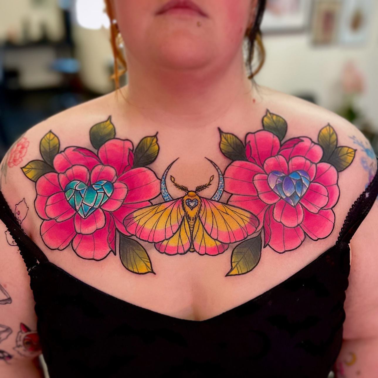 Colorful tattoo of a moth and two large flowers on person's chest, with leaves and detailed petals.