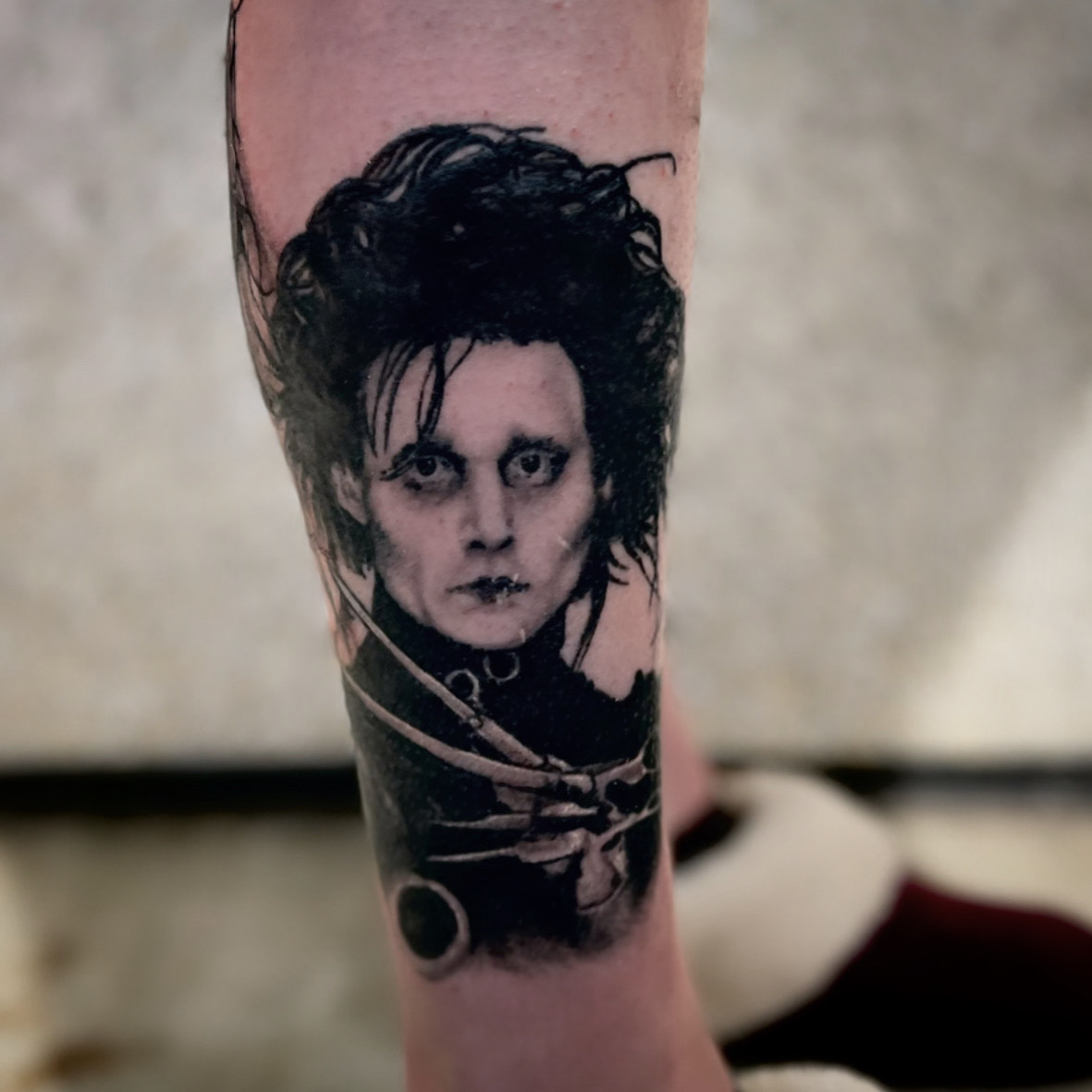 Tattoo of a person with dark, messy hair and pale face on a person's arm.