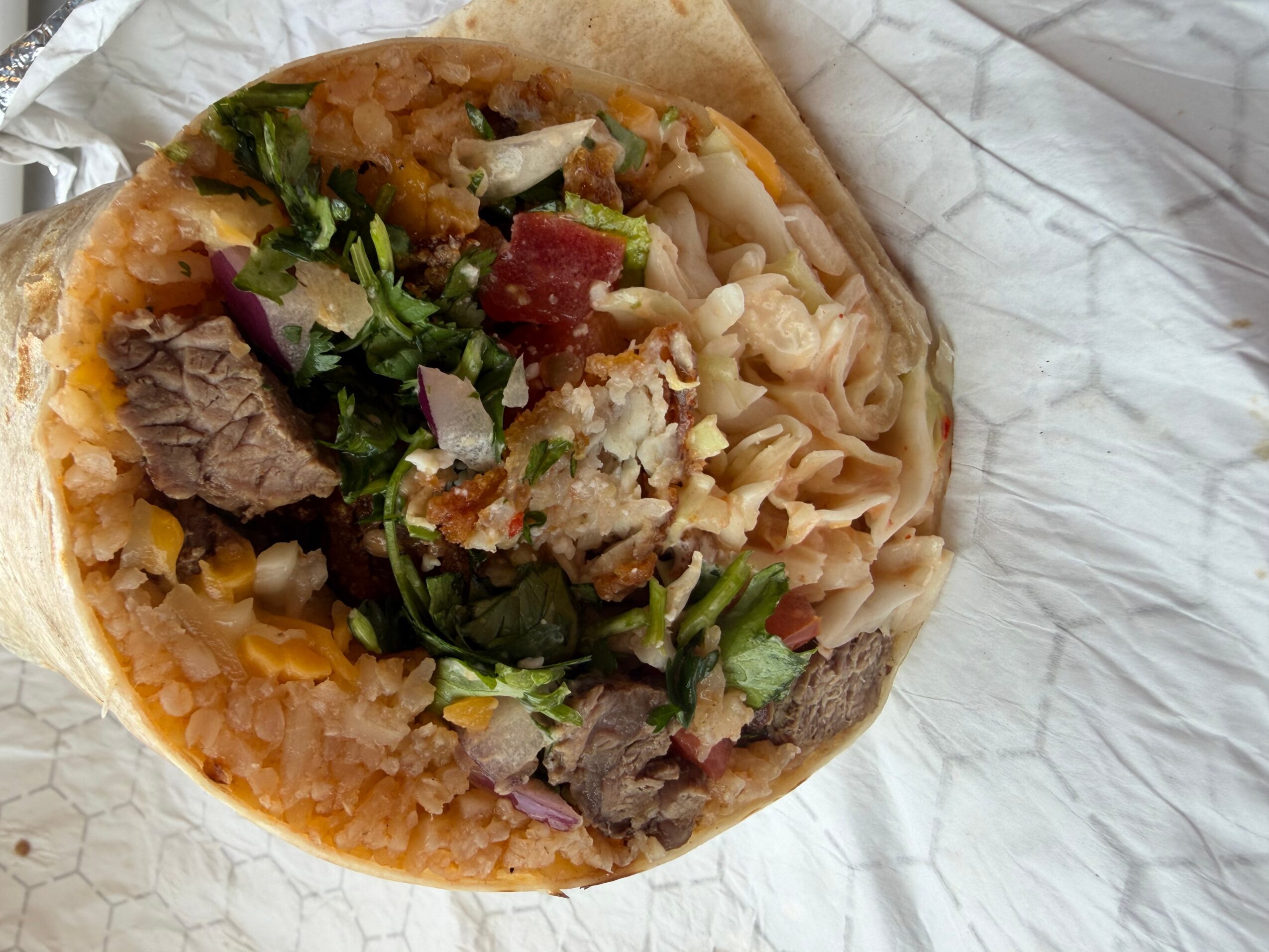 A bowl of ramen with noodles, meat, vegetables, and broth, placed on crumpled white paper.