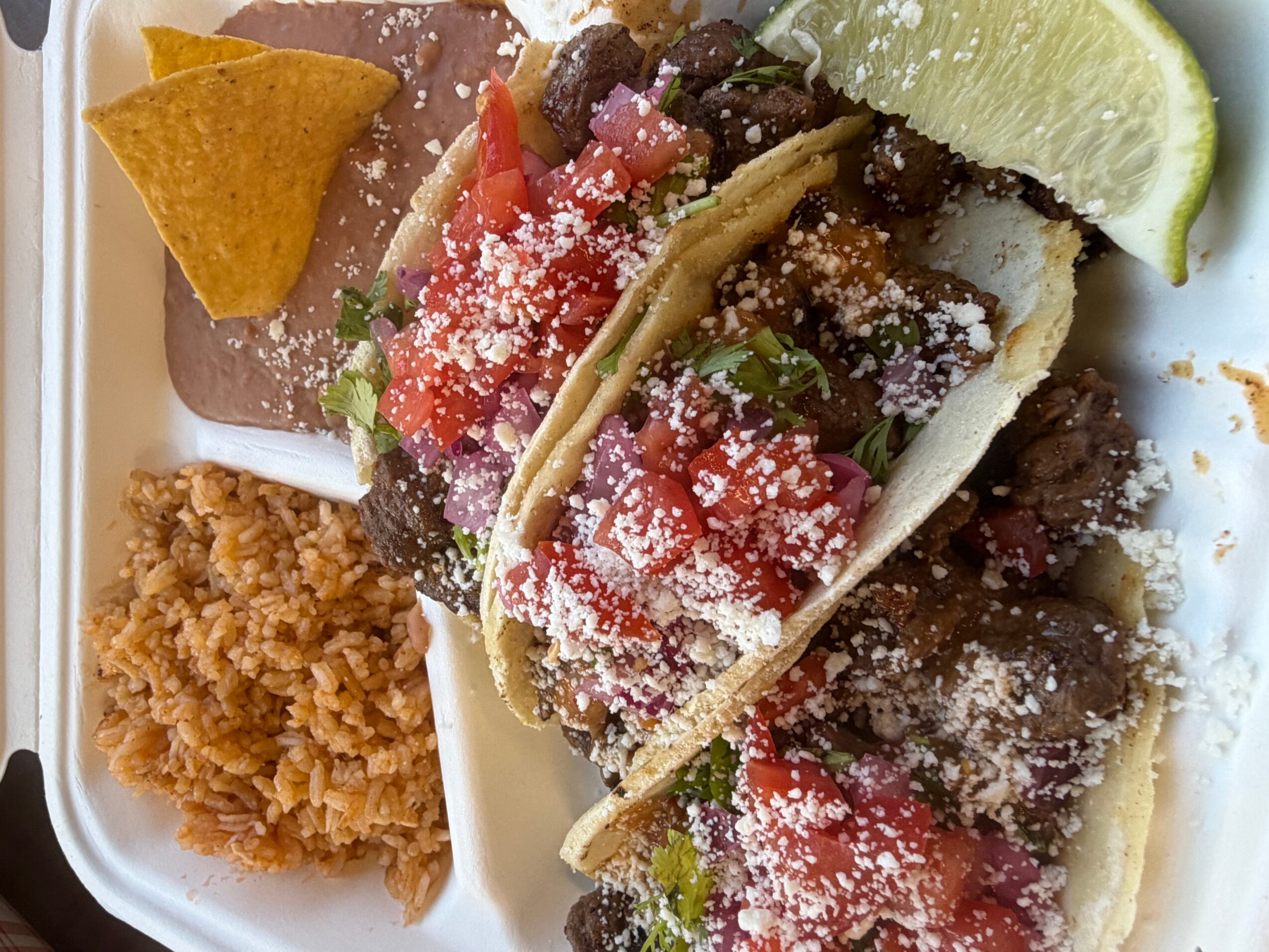 Plate with tacos, rice, and chips, garnished with lime and cheese, on a white tray.