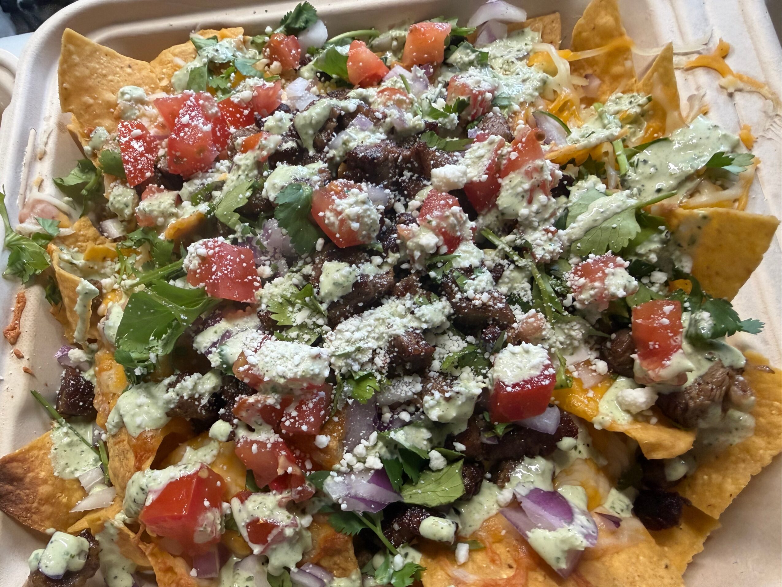 Tortilla chips topped with lettuce, tomatoes, onions, black beans, cheese, and cilantro, garnished with grated cheese.
