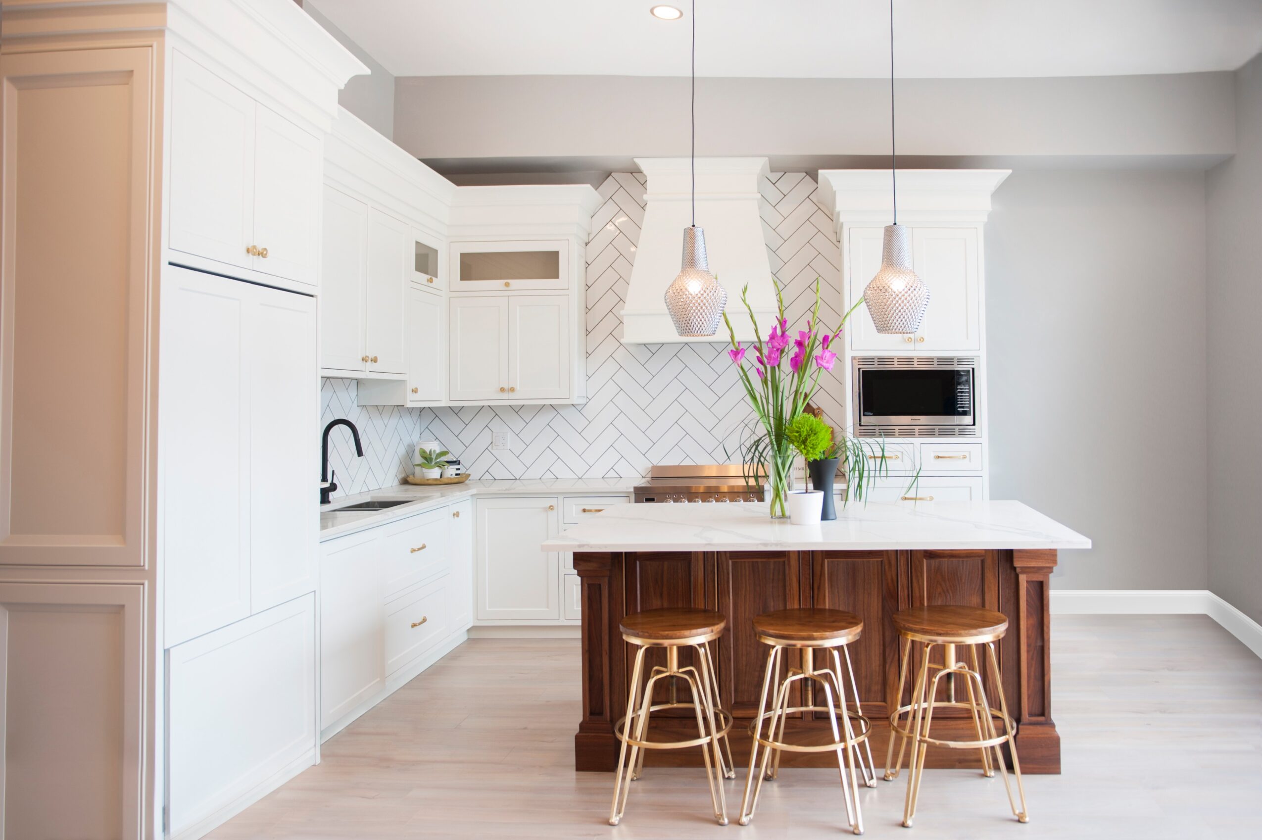Modern kitchen with white cabinets, a central island with three stools, and pink flowers in a vase, bright and airy.