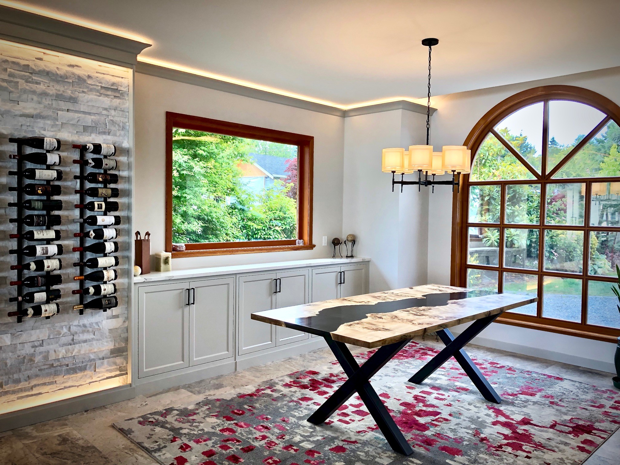 Dining room with large arched window, white cabinetry, and a table with a marble top, rug, and chandelier.