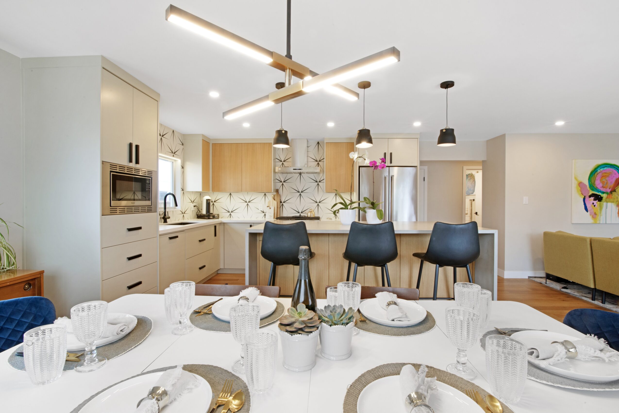 Open kitchen and dining area with a table set for a meal, modern lighting, and colorful artwork on the wall.