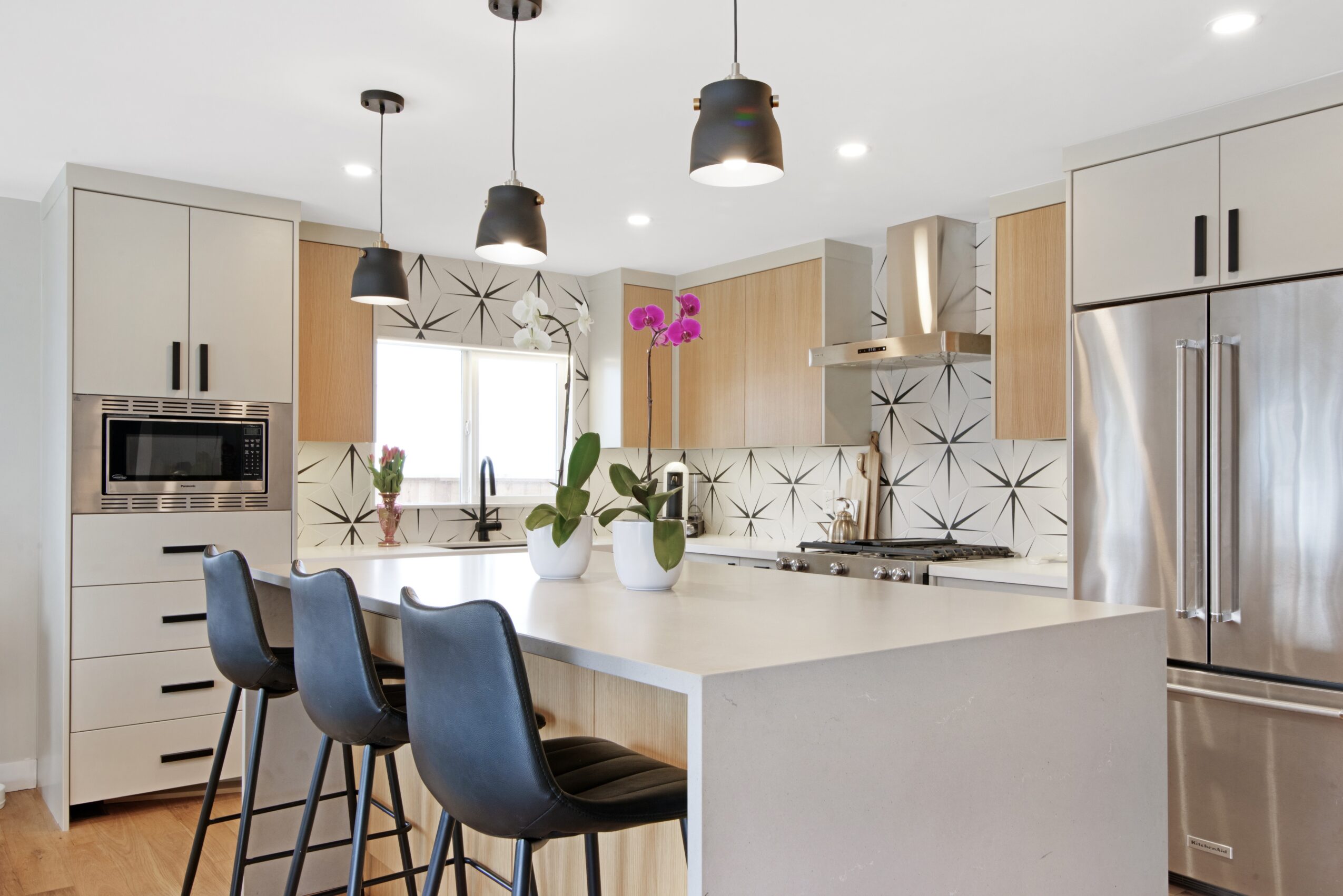 Modern kitchen with white cabinets, stainless steel appliances, black pendant lights, and a large island with three black chairs.