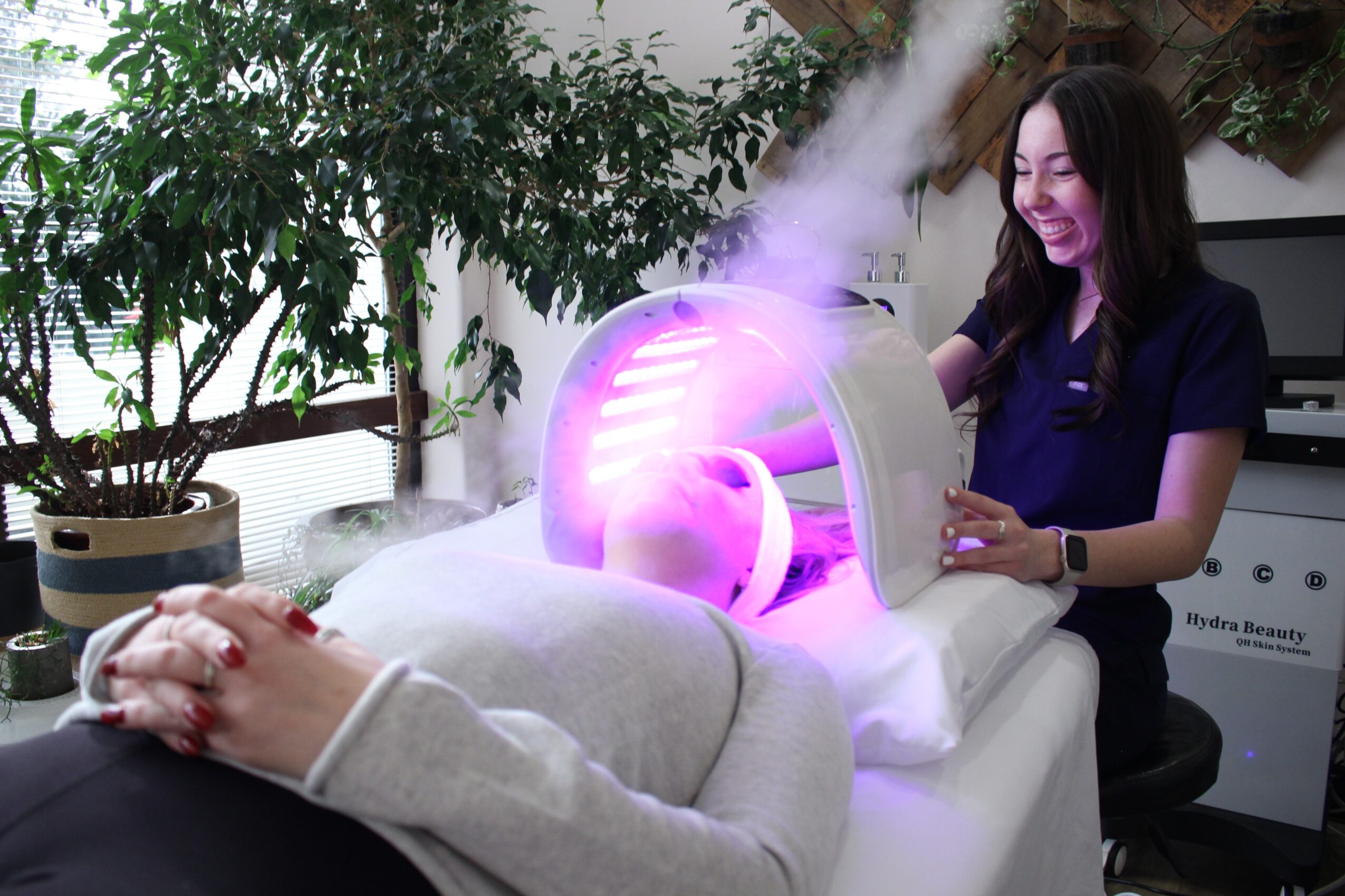 A woman receives a facial treatment with a device emitting purple light and steam, in a spa setting.