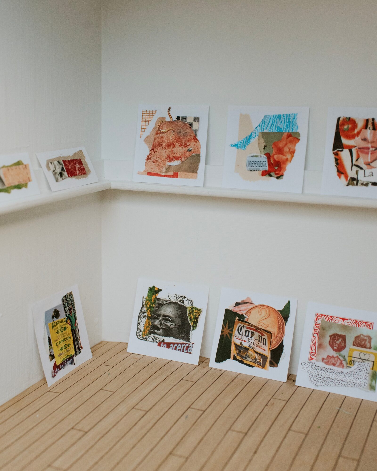 Photographs of various artworks or posters displayed on white walls and a wooden floor, arranged on shelves and the floor.