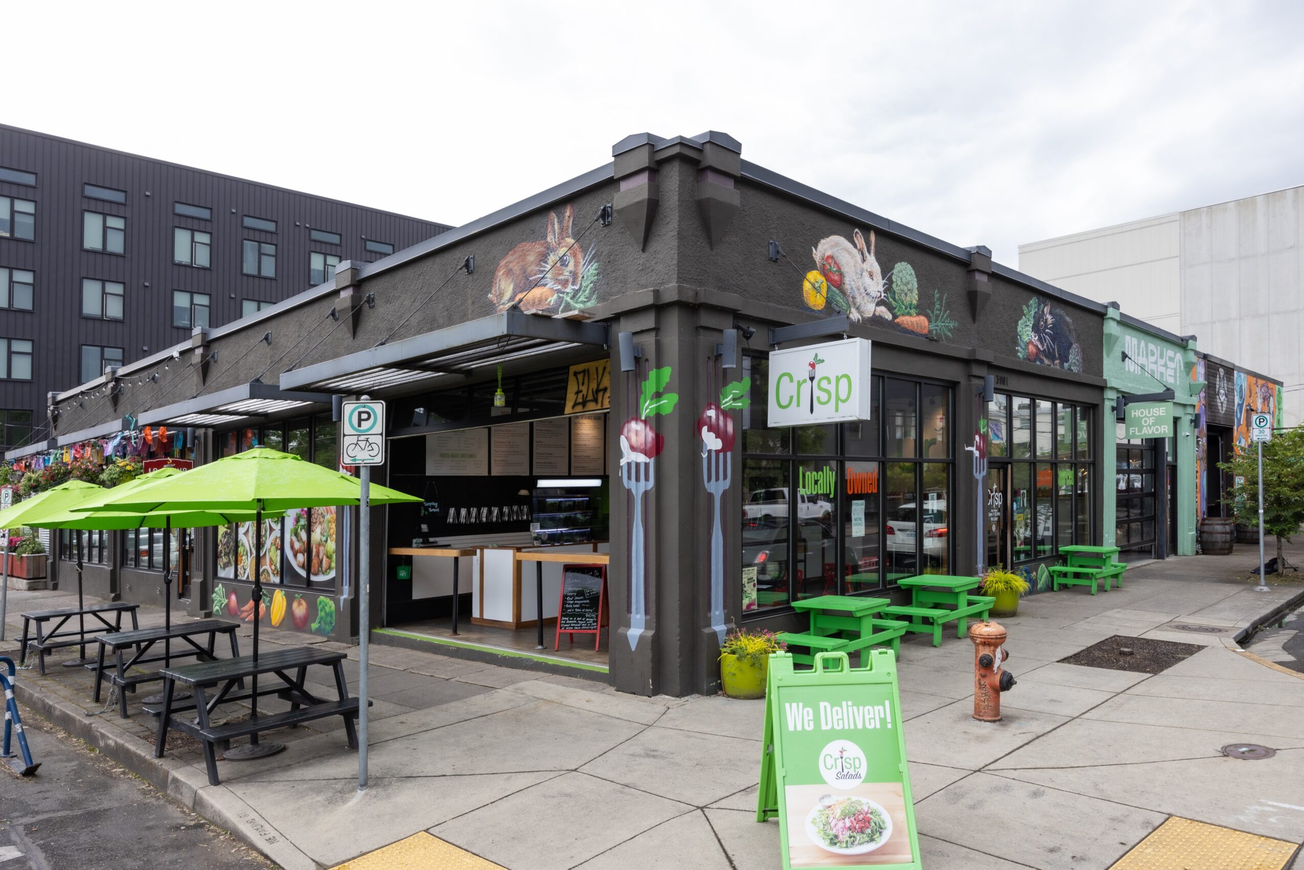Corner view of a restaurant with outdoor seating, green umbrellas, and colorful graffiti on the building exterior.