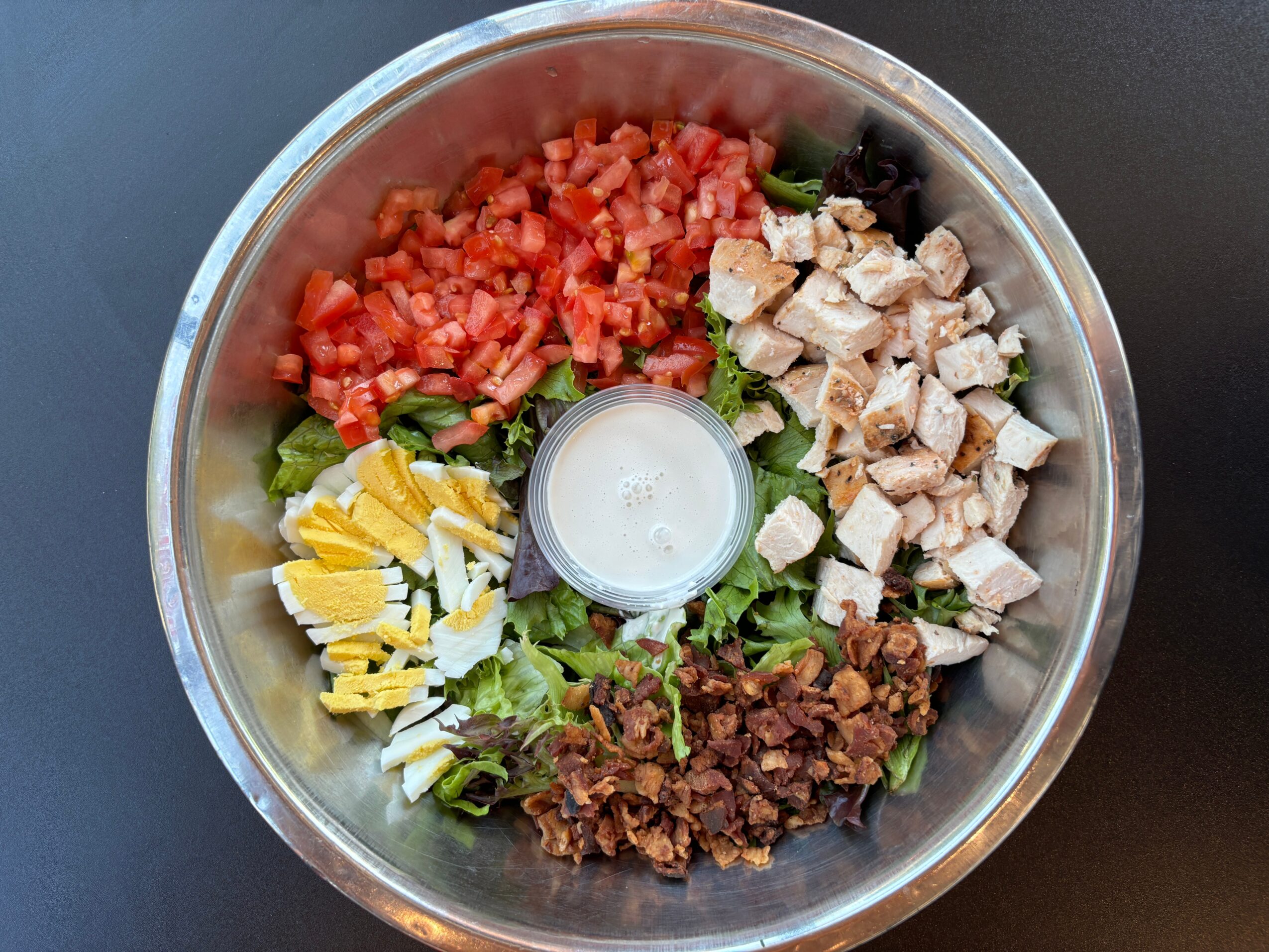 Bowl with chopped tomatoes, diced chicken, shredded cheese, cooked ground meat, and chopped lettuce, with a small container in the center.