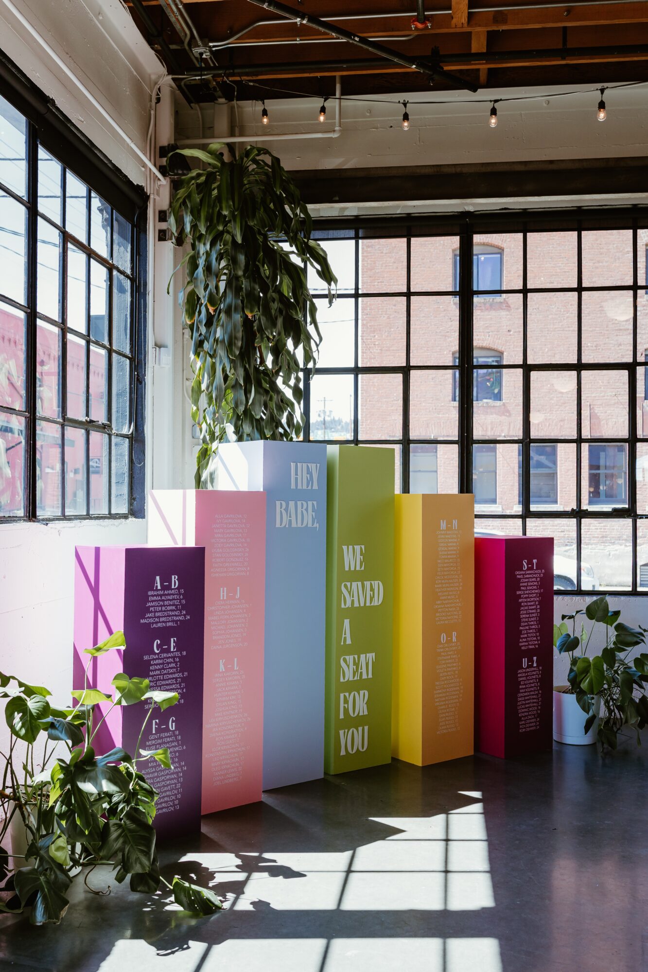 Colorful books arranged in a row on a windowsill with plants and large windows showing buildings outside.