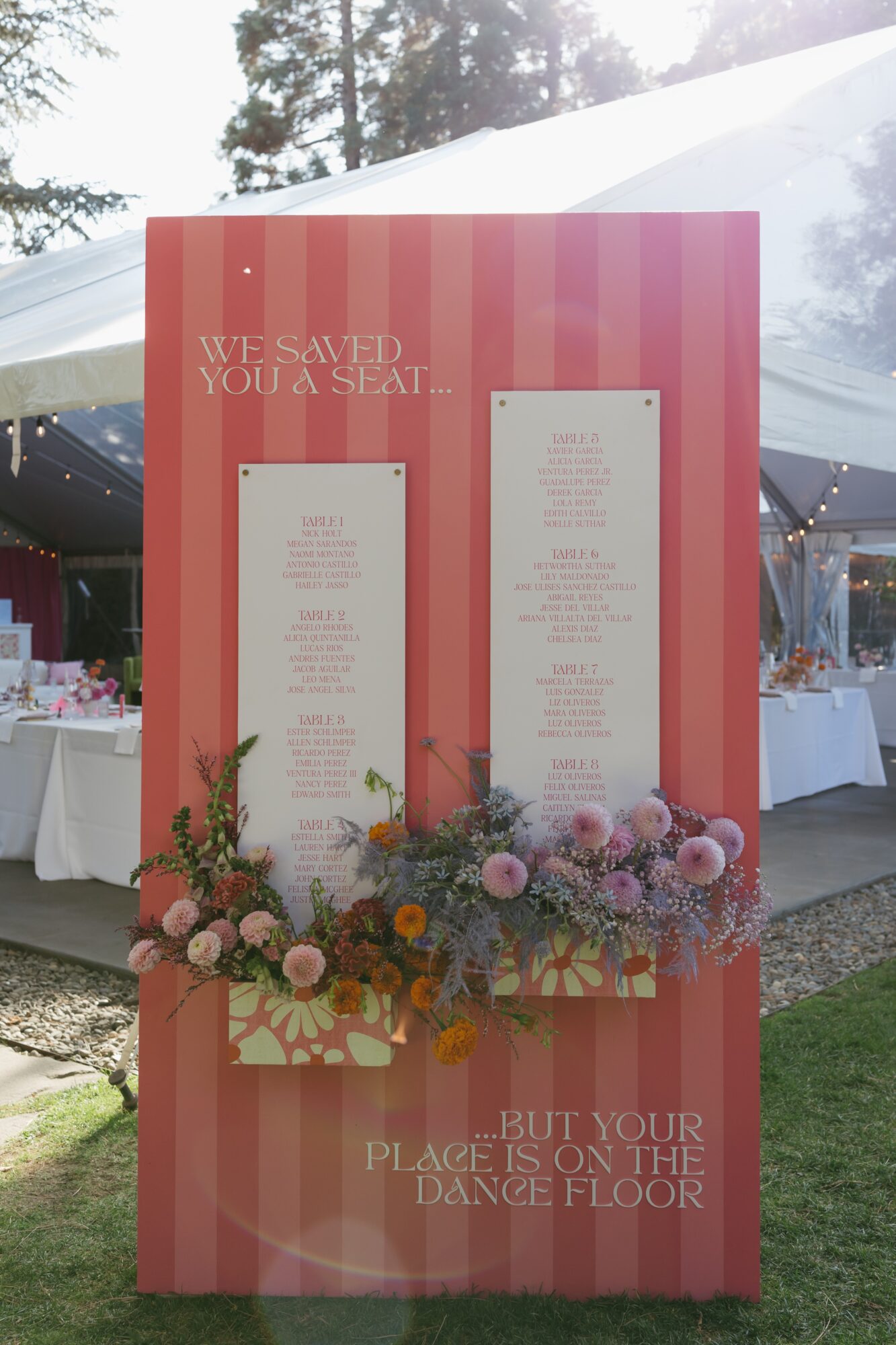 Pink striped wedding sign with floral decorations at the bottom, displaying seating and dance floor instructions.