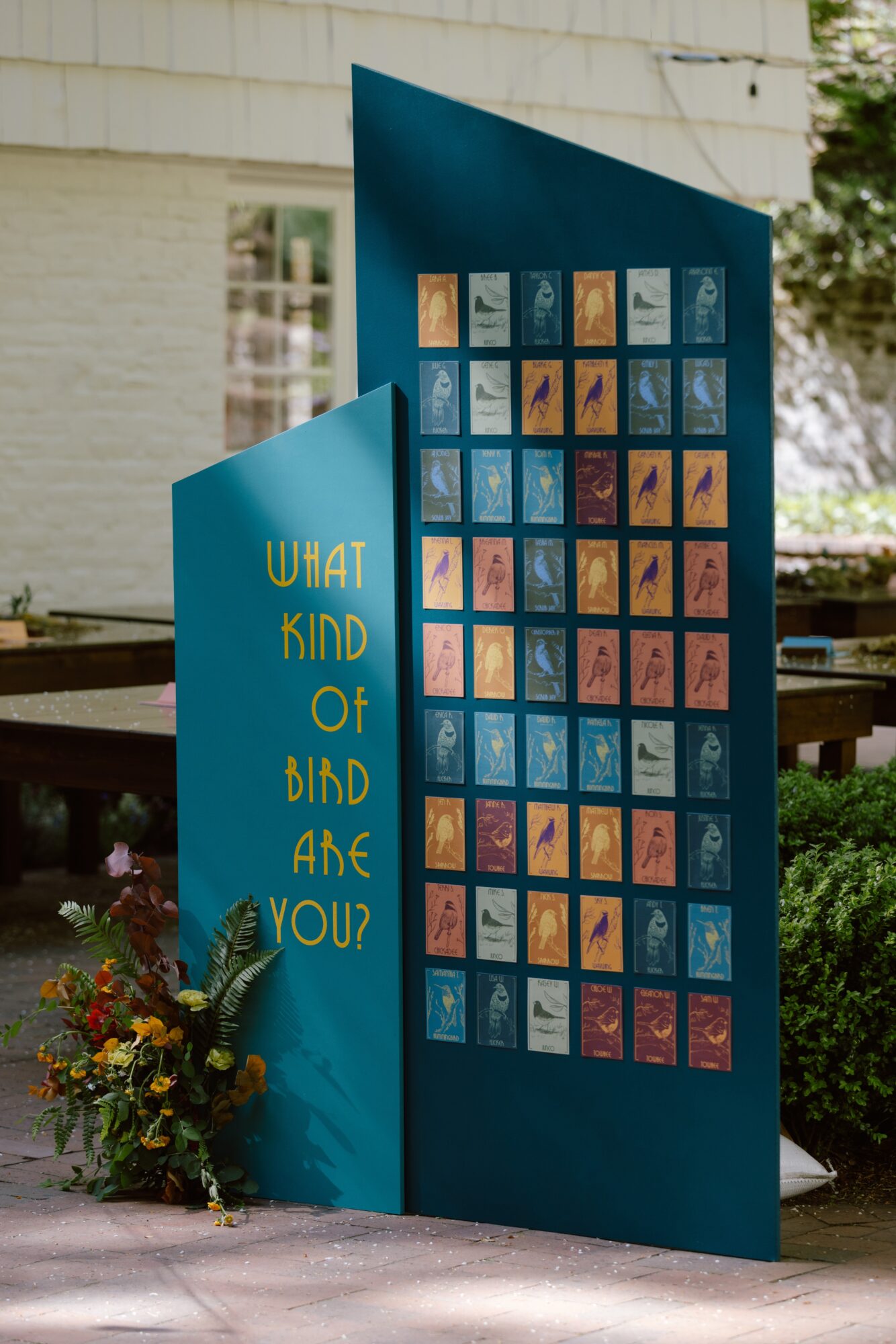Blue display with text 'What kind of bird are you?' and colorful bird illustrations, outdoors near a building and greenery.