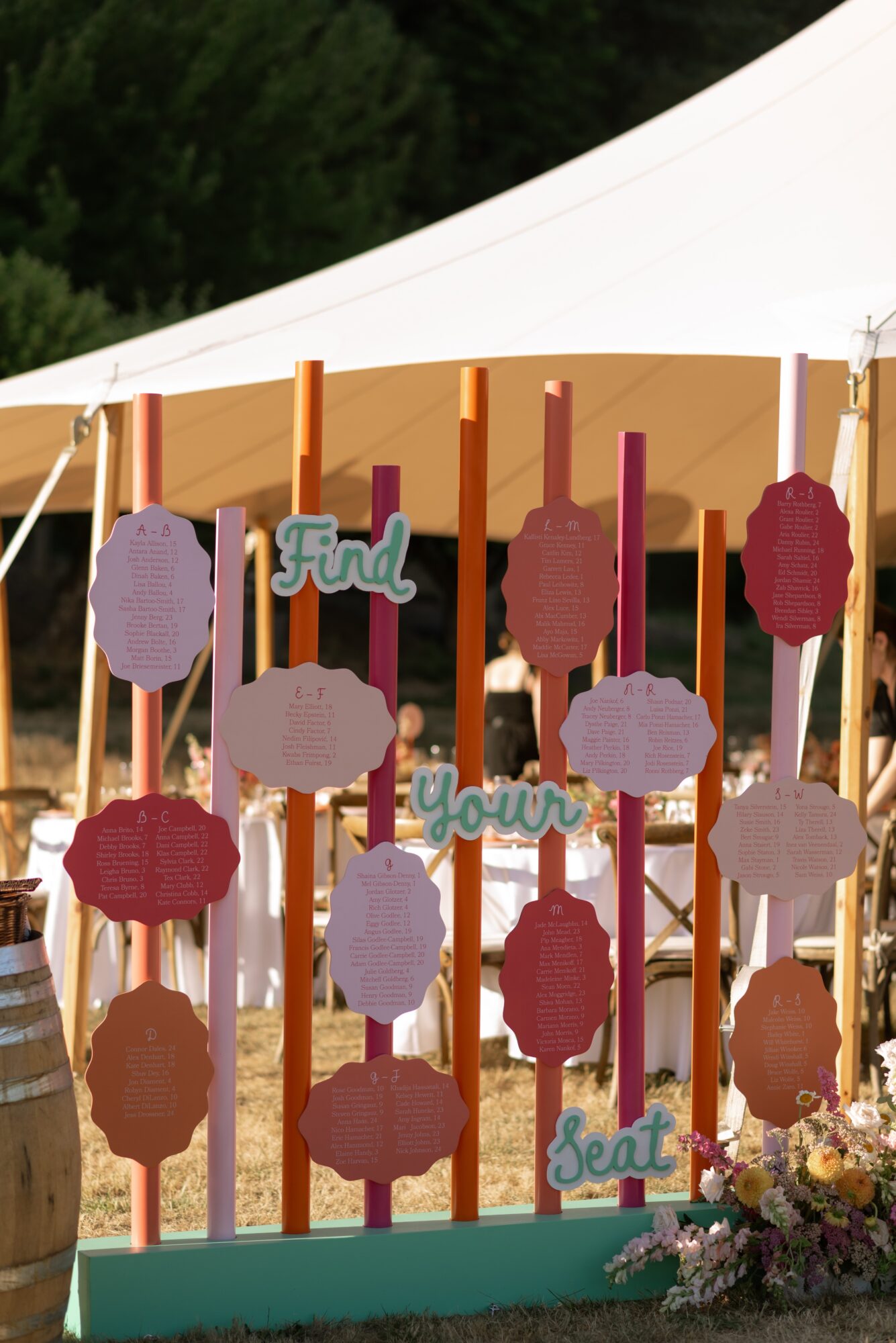 Display with pink, purple, and beige paper notes on sticks, decorated with flowers at the base, outdoors under a tent.