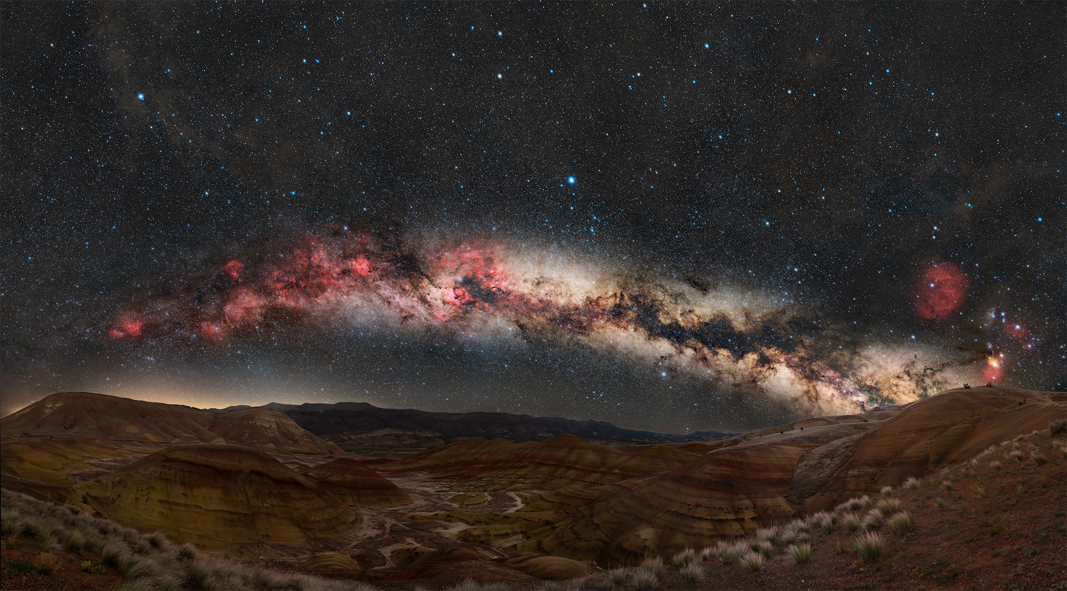 Night sky with the Milky Way galaxy visible above a landscape of hills and sparse vegetation.