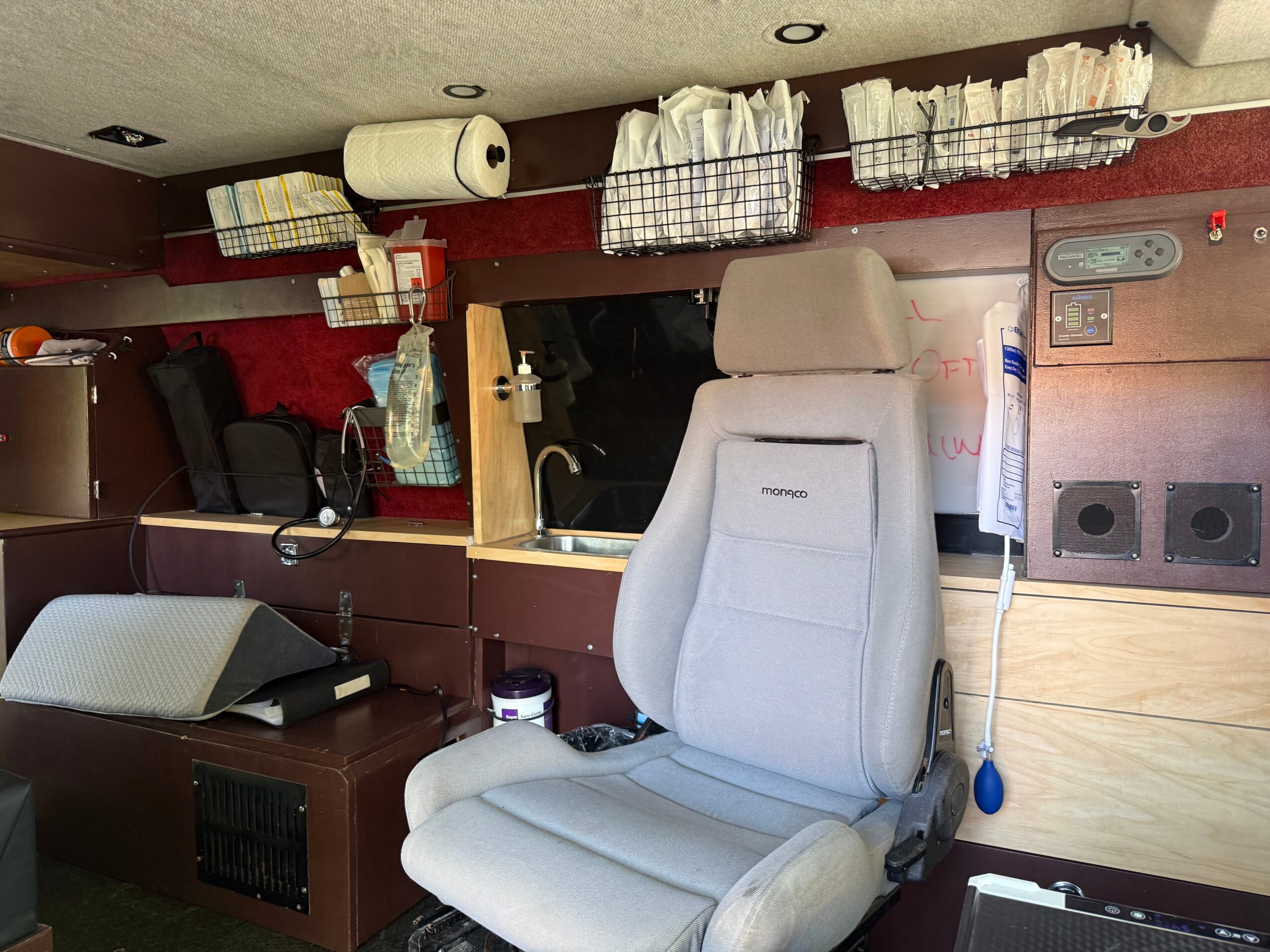 Medical or dental office with a white chair, shelves with supplies, and equipment on the wall.