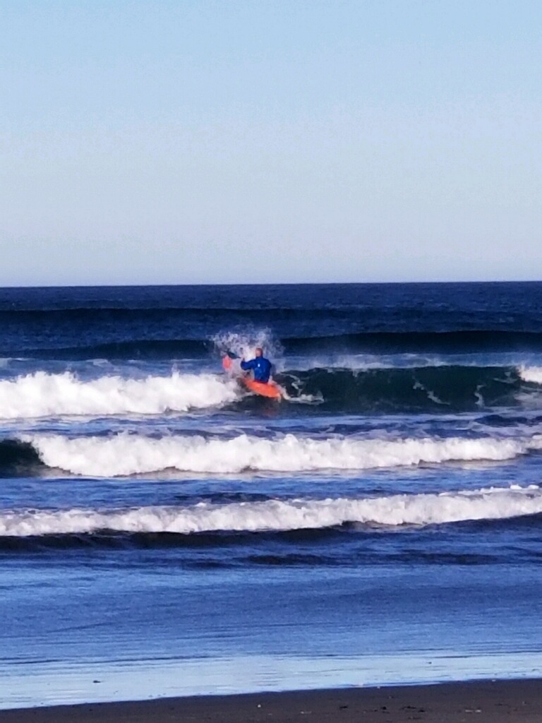 Person riding a surfboard on ocean waves with a clear sky background.