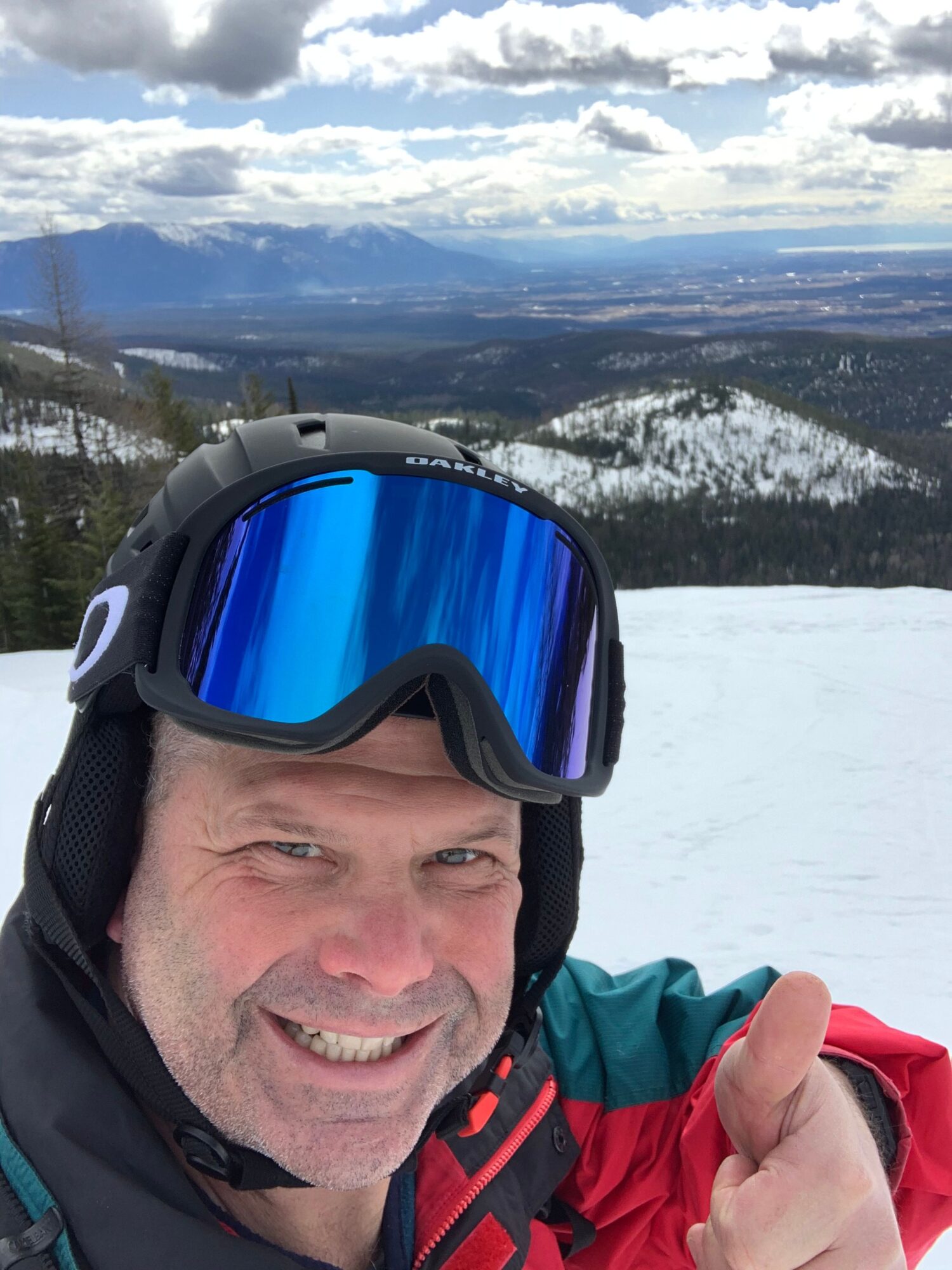 Person in ski gear taking a selfie with snowy mountain landscape and sky in background.