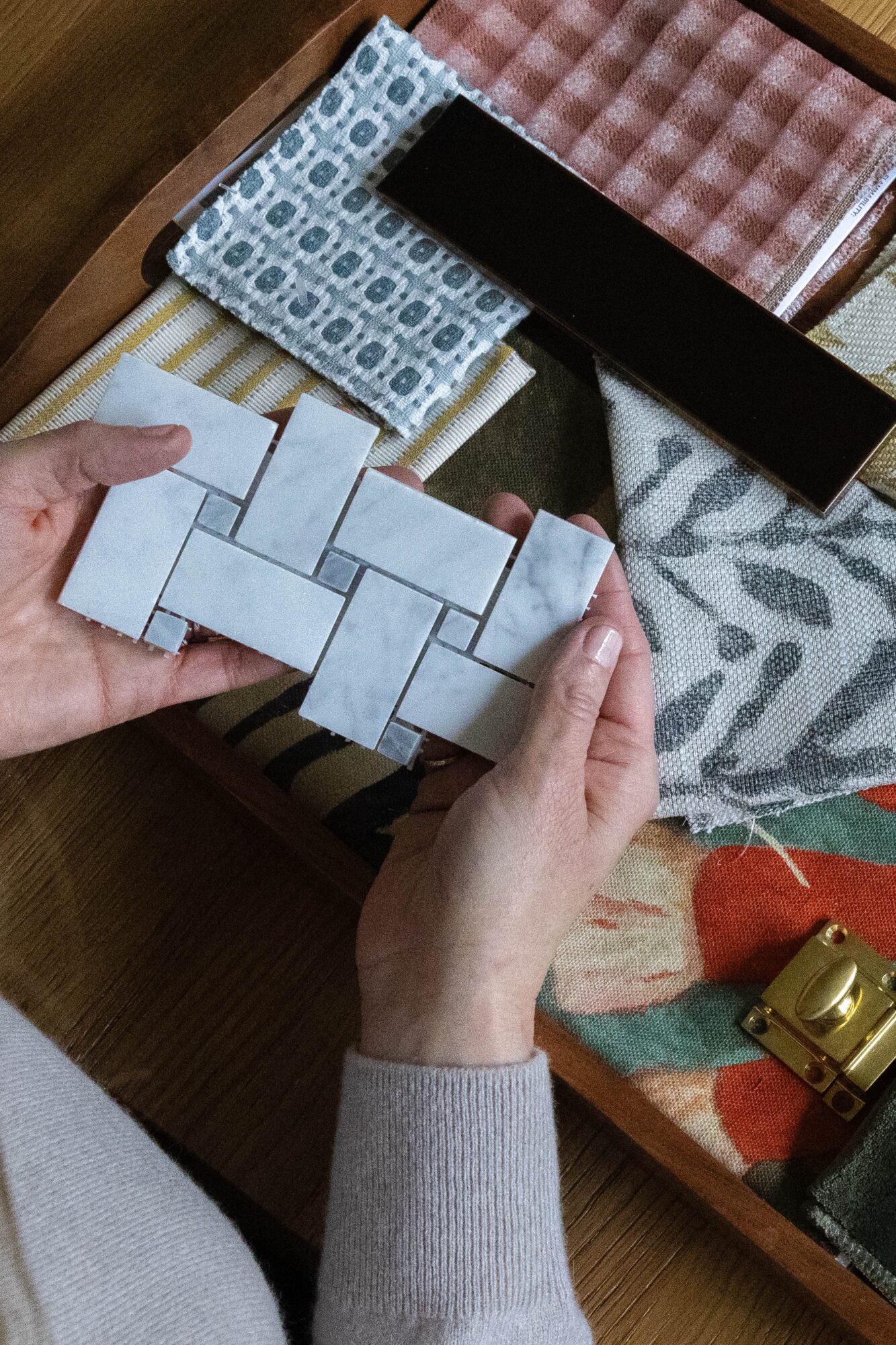 Person holds small white tile pieces over fabric samples on a table.