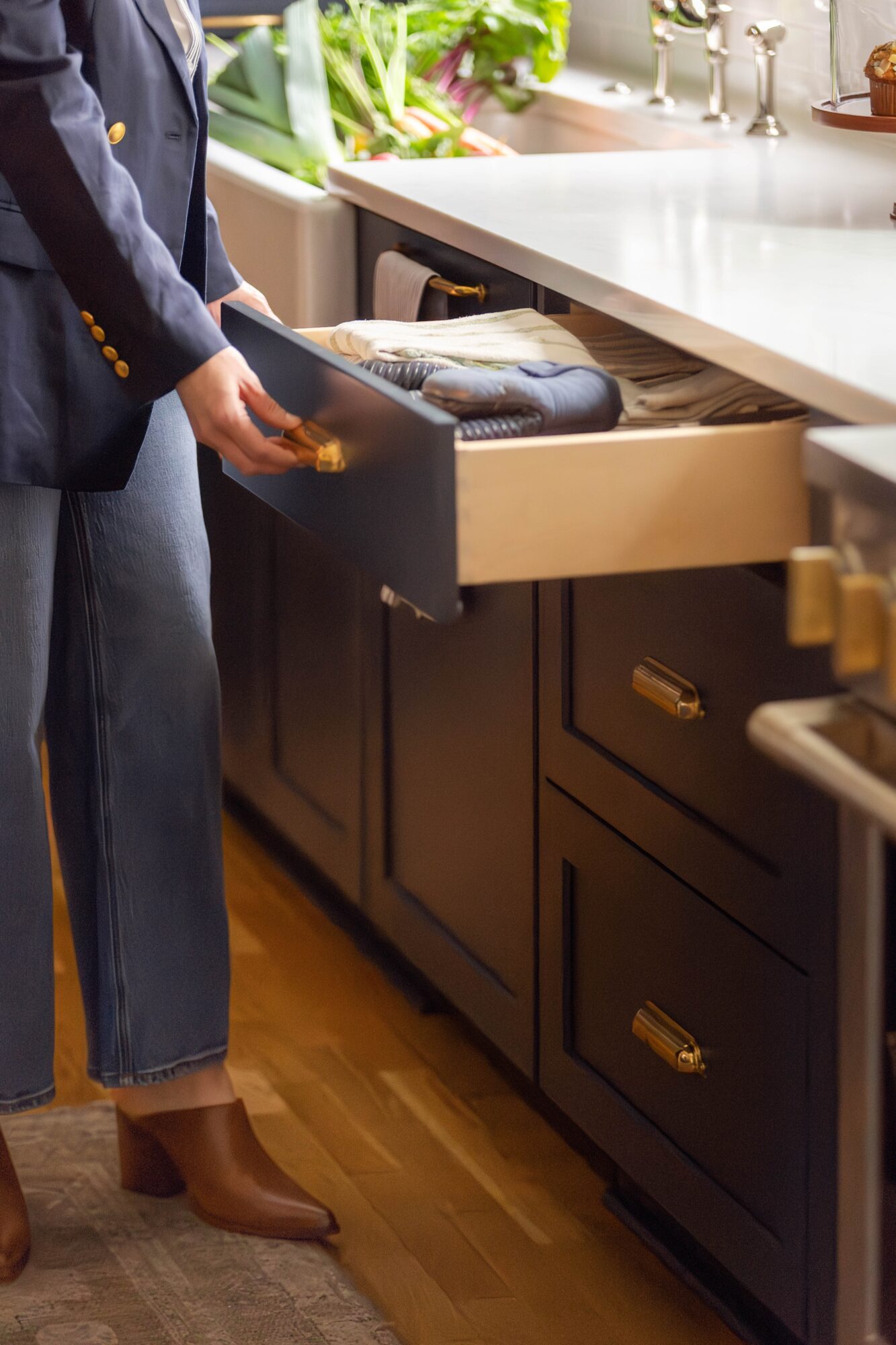 Person opening a kitchen drawer with utensils and a cutting board inside, near a white countertop and dark cabinets.