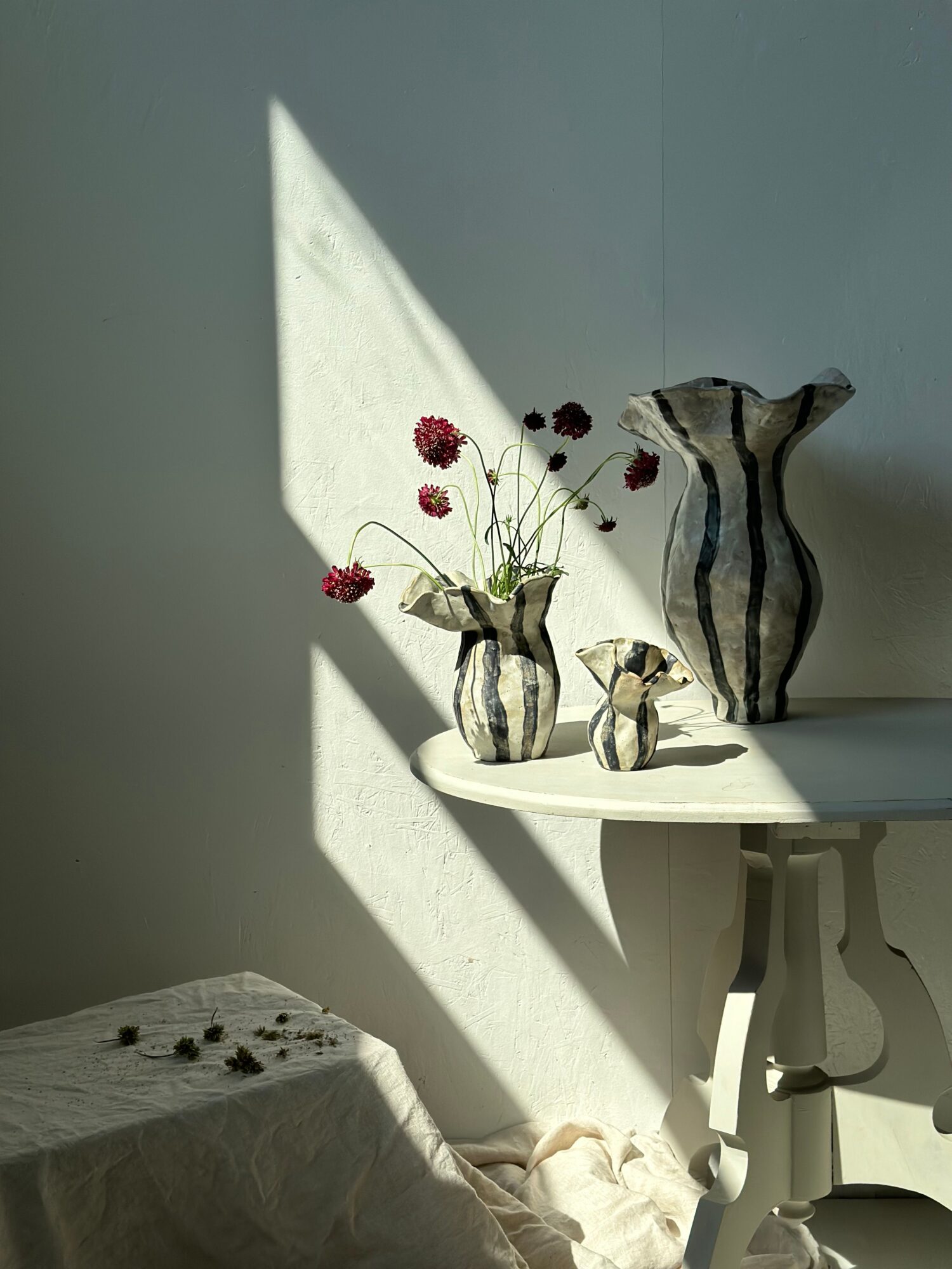 A striped fabric bag with red flowers and green stems on a white surface, illuminated by sunlight, with shadows cast.