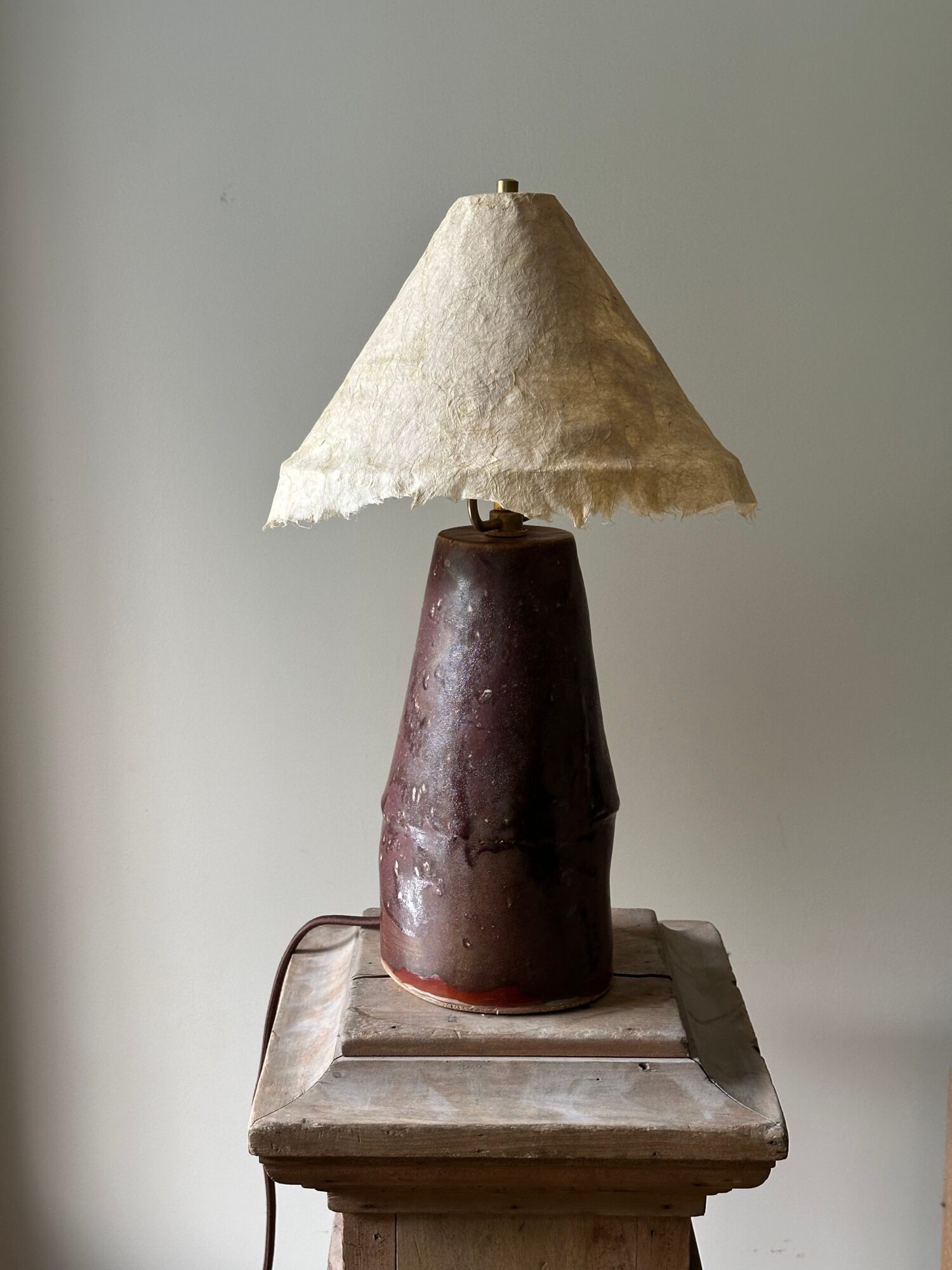 Object with a conical fabric shade, a cylindrical base, and a wooden platform, viewed sideways.
