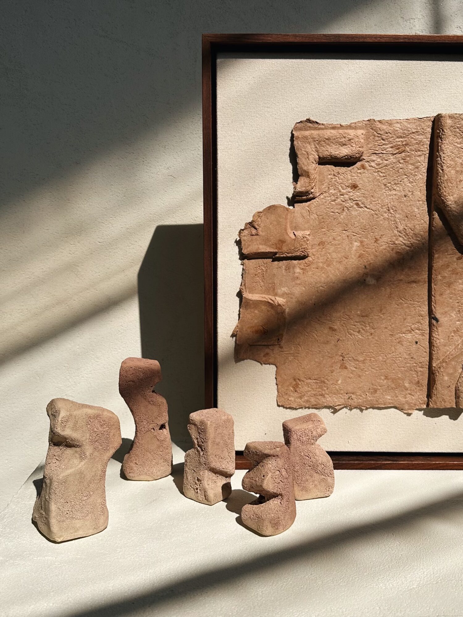 Ancient clay tablets and small clay figurines arranged on a surface with shadows, framed by a shadowed wall.