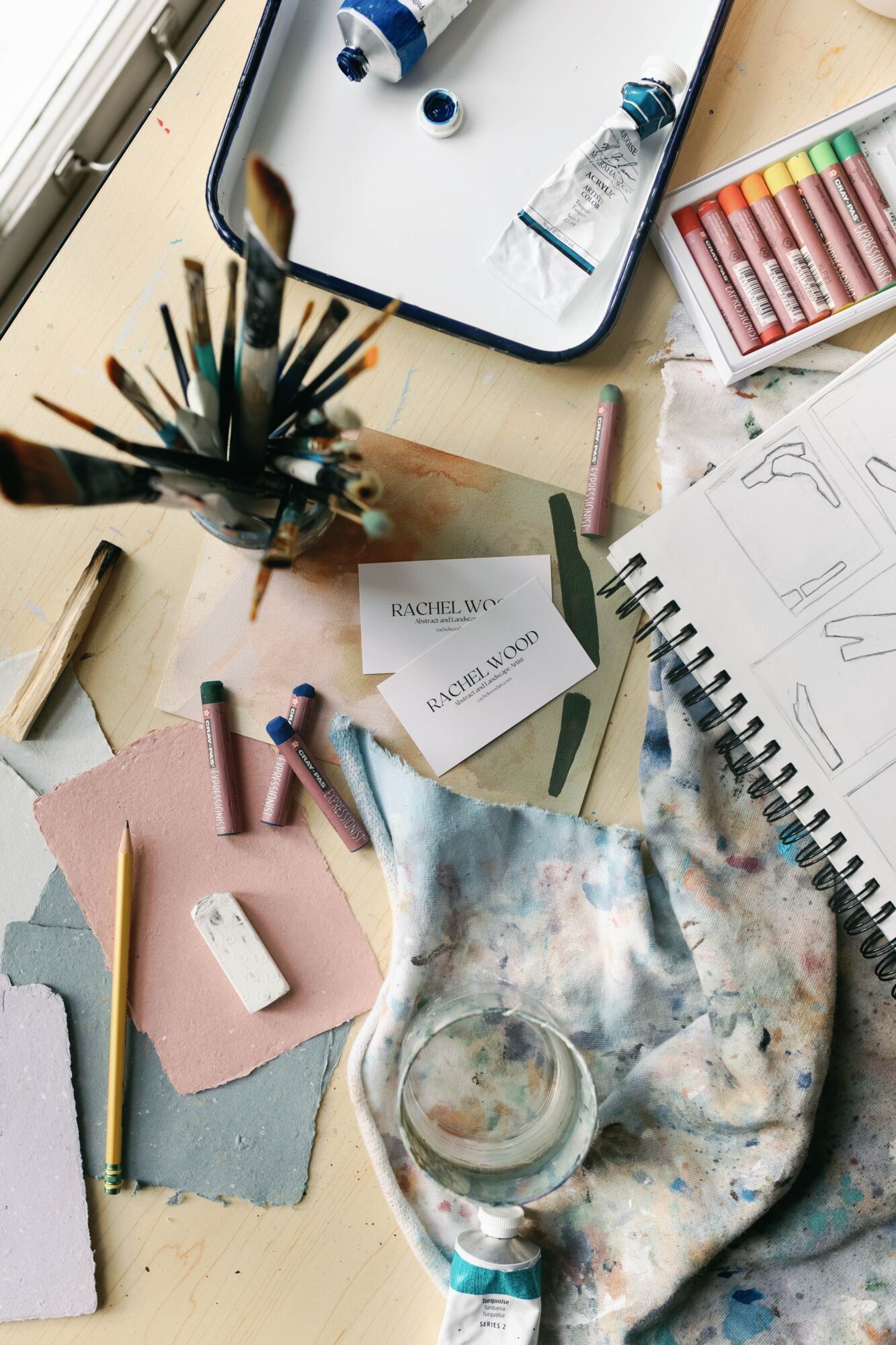 Art supplies including brushes, paints, paper, and sketches on a cluttered table.
