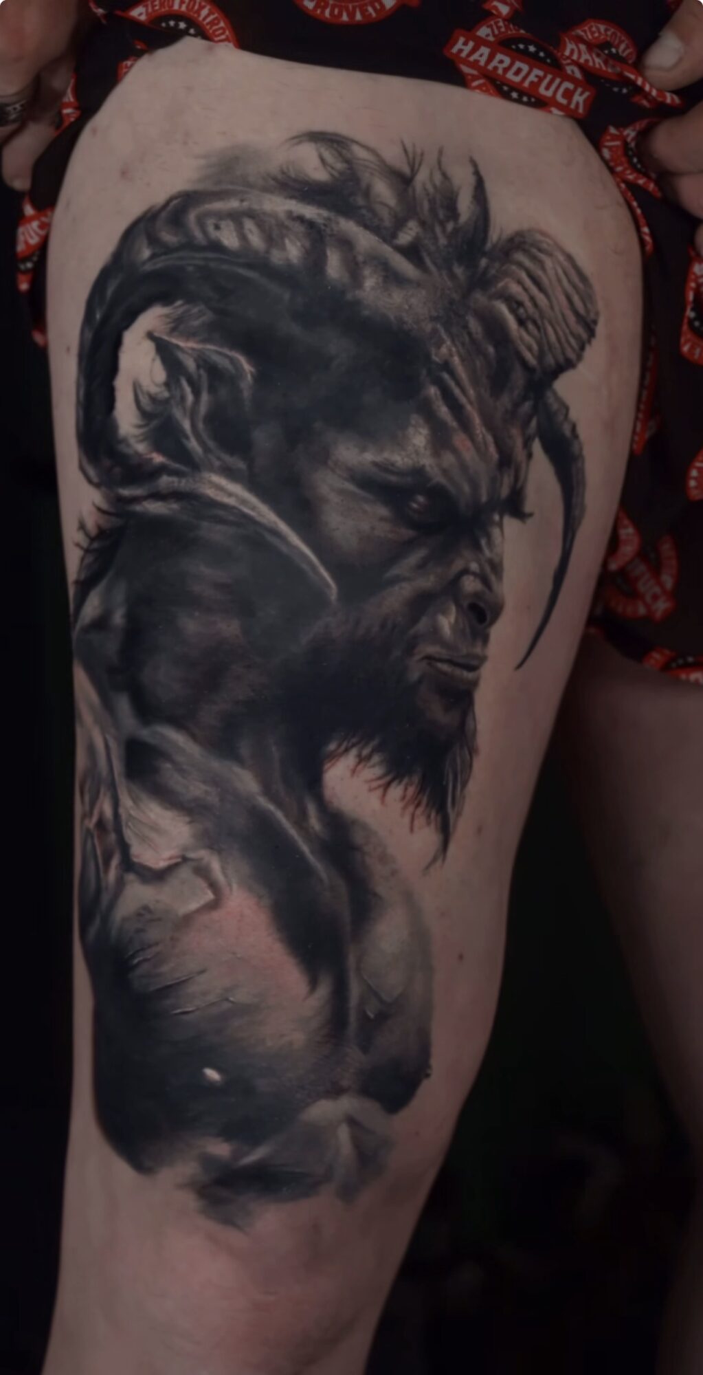 Detailed black and gray tattoo of a lion's face with a mane, blending into a dark background on a person's thigh.
