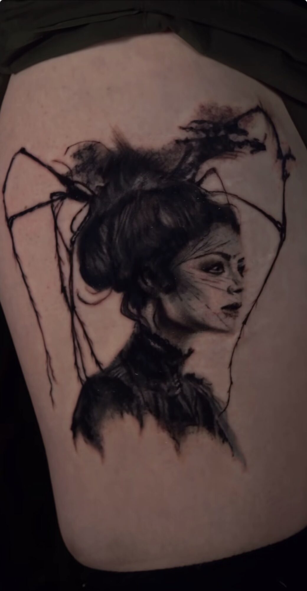Tattoo of a woman with dark hair and spider-like elements on her head and shoulders.