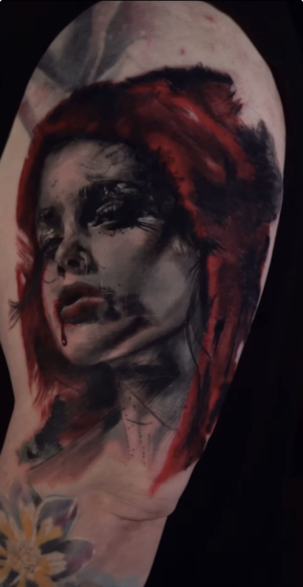 Tattoo of a woman's face with red hair, detailed shading, and a floral design near the shoulder.