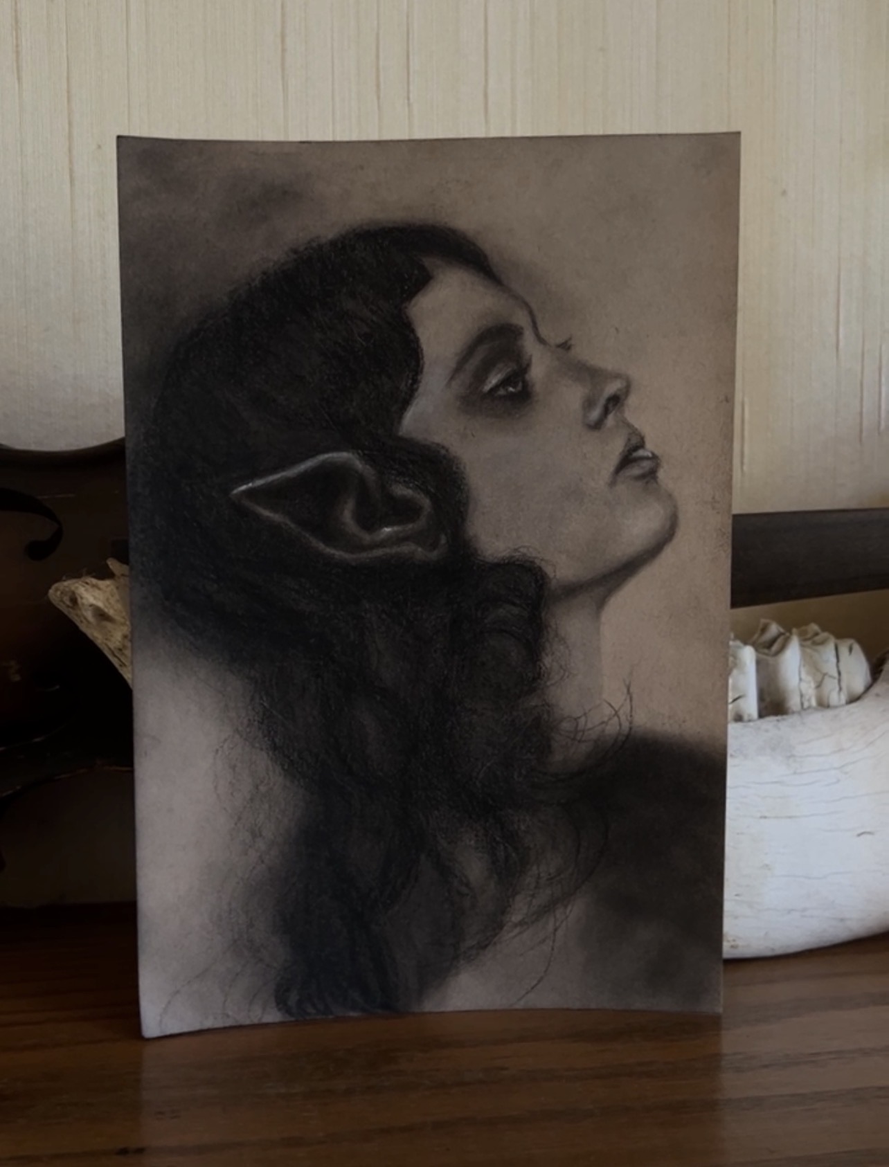 Black and white drawing of a woman with elf-like ears, her head tilted upward, with long dark hair and detailed facial features.