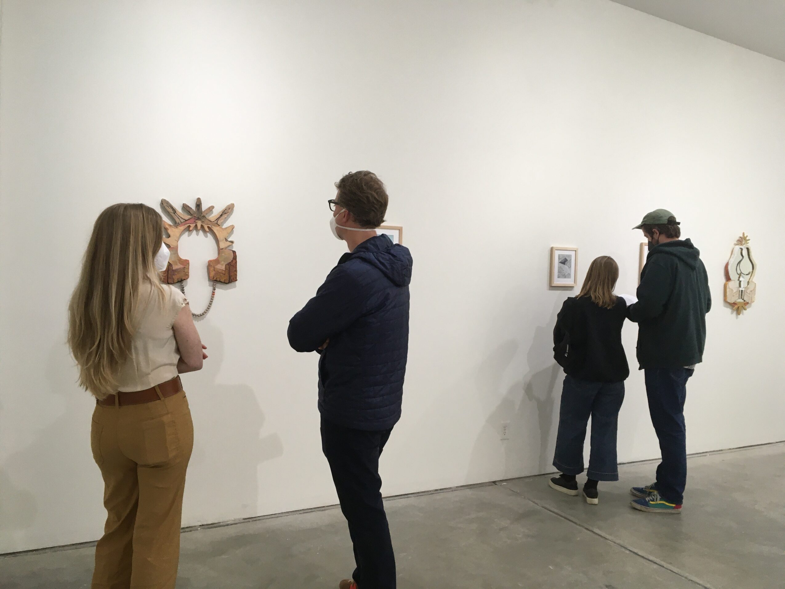 People viewing artwork in a gallery, with some looking at wall-mounted pieces and discussing them.