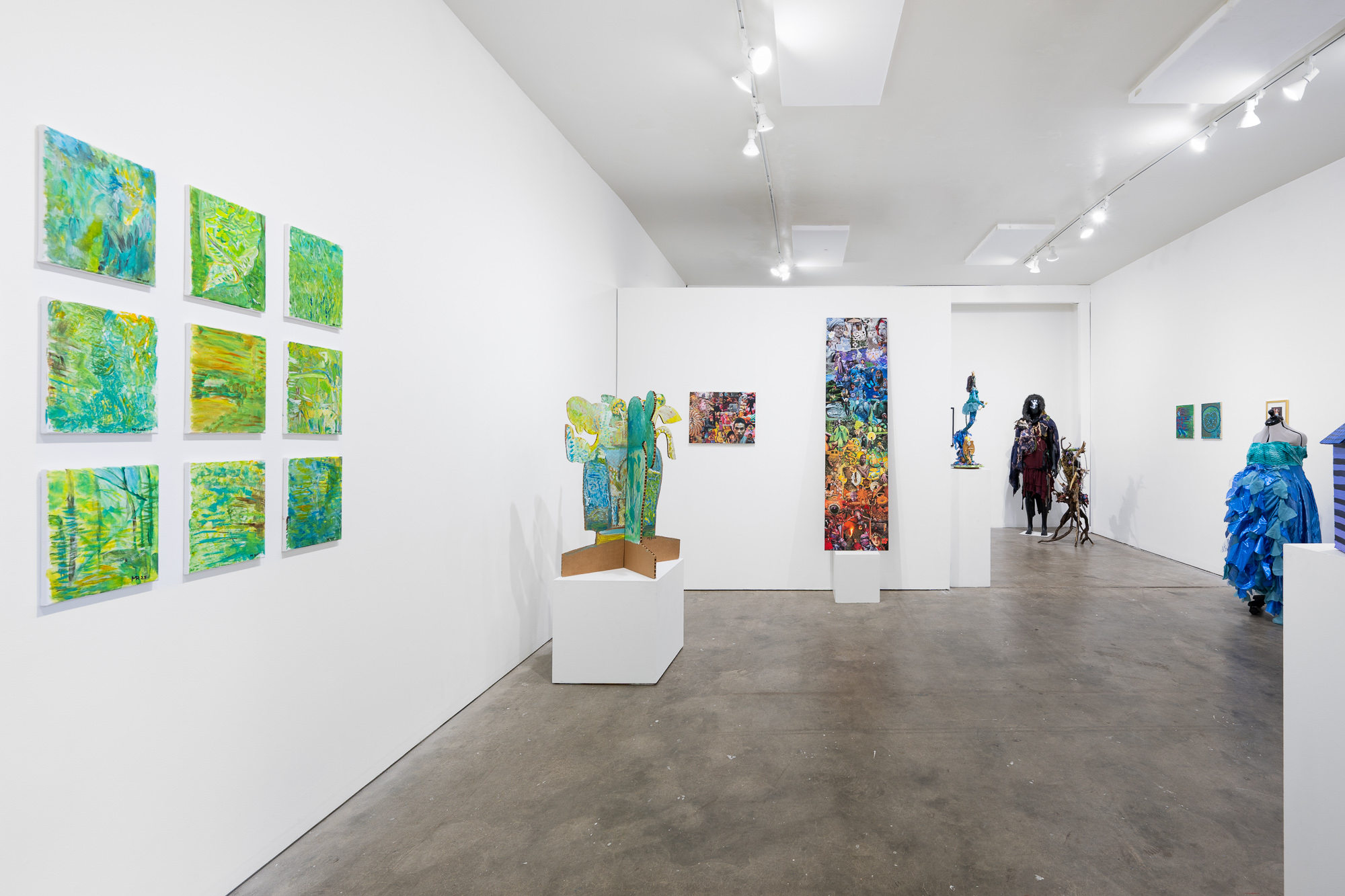 Art gallery with colorful paintings and sculptures displayed on white walls and pedestals, with a horse sculpture and a blue dress in the background.