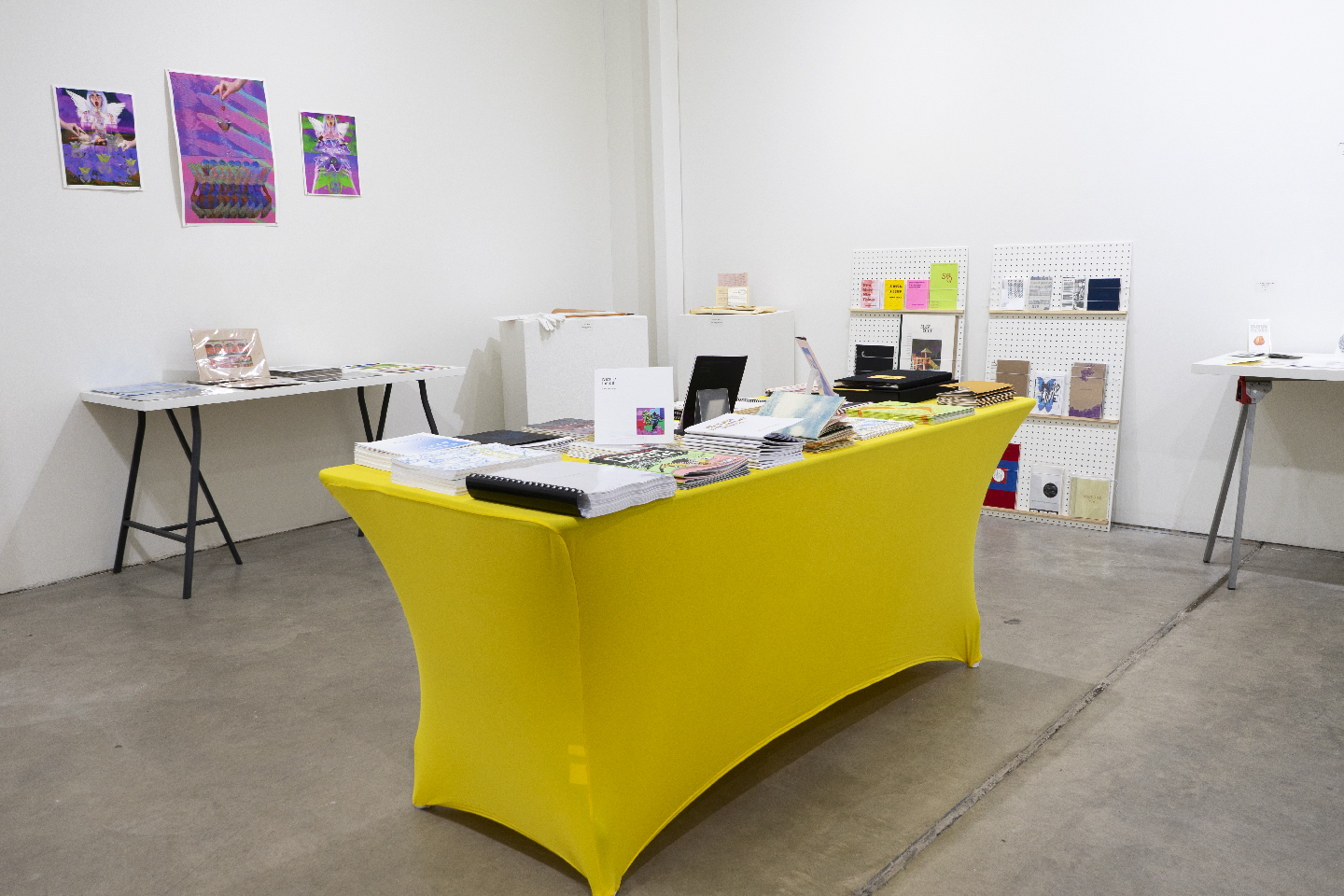 Office space with a yellow desk, white walls, and colorful artwork on the wall, with various office supplies on the desk.