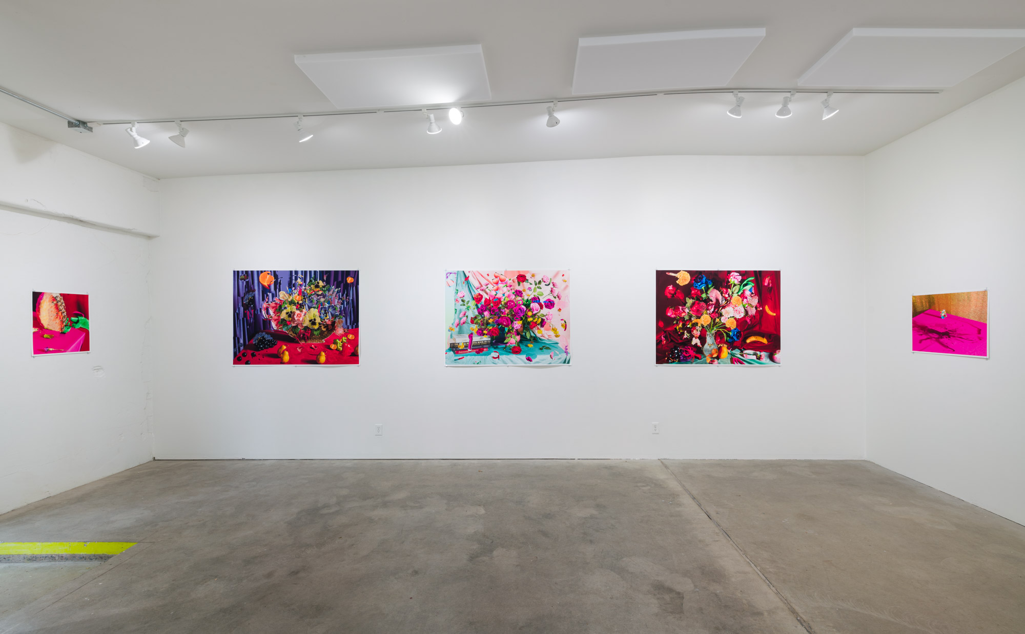 Gallery with five colorful paintings on white walls, concrete floor, ceiling lights, and a yellow object on the floor.
