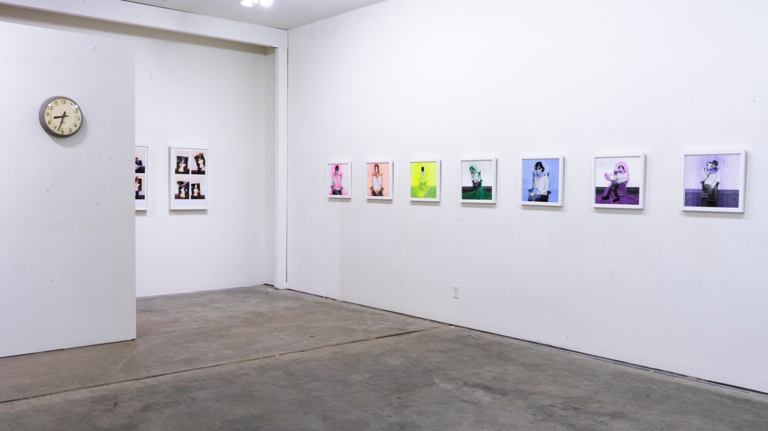 Gallery with white walls, concrete floor, and framed colorful artworks displayed in a row.