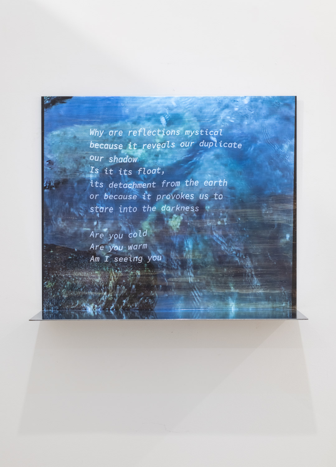 Abstract blue painting with white text overlay, displayed on a white wall, casting a shadow below.