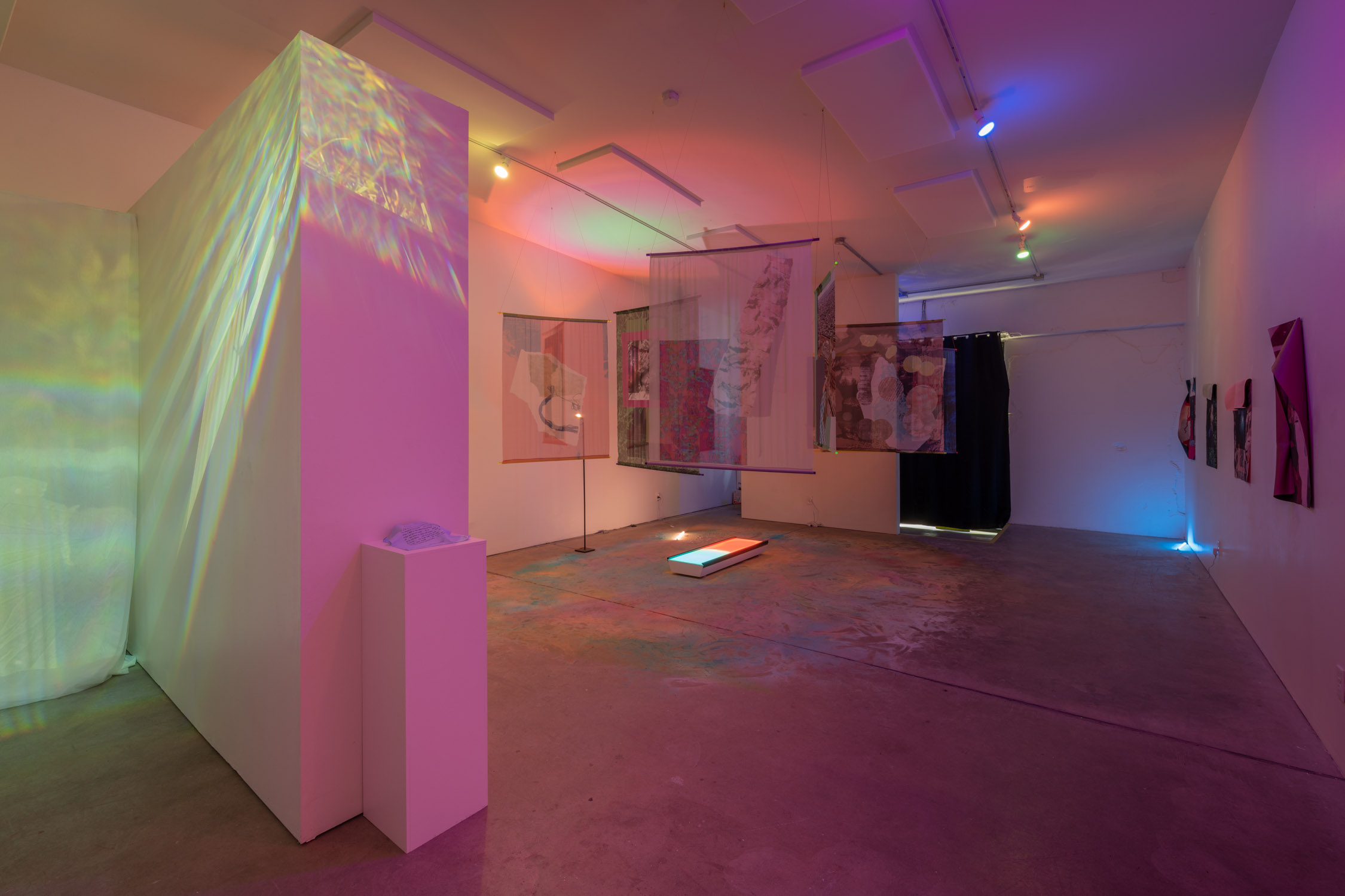 Art gallery with colorful lighting, hanging artworks, and a projection on a wall, with a polished floor and white walls.