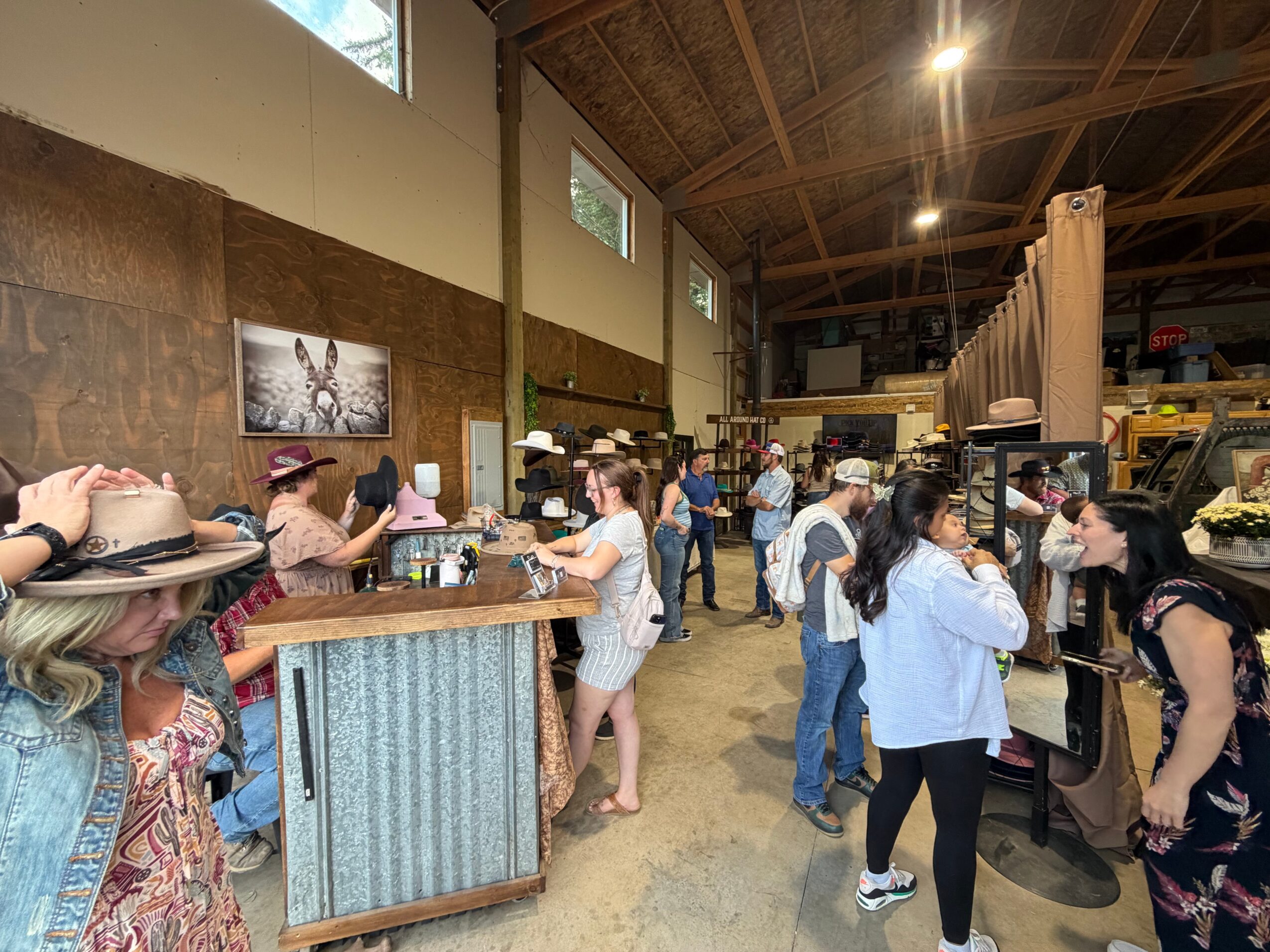 People gather at a market or event inside a large industrial-style building with high ceilings and wooden beams.