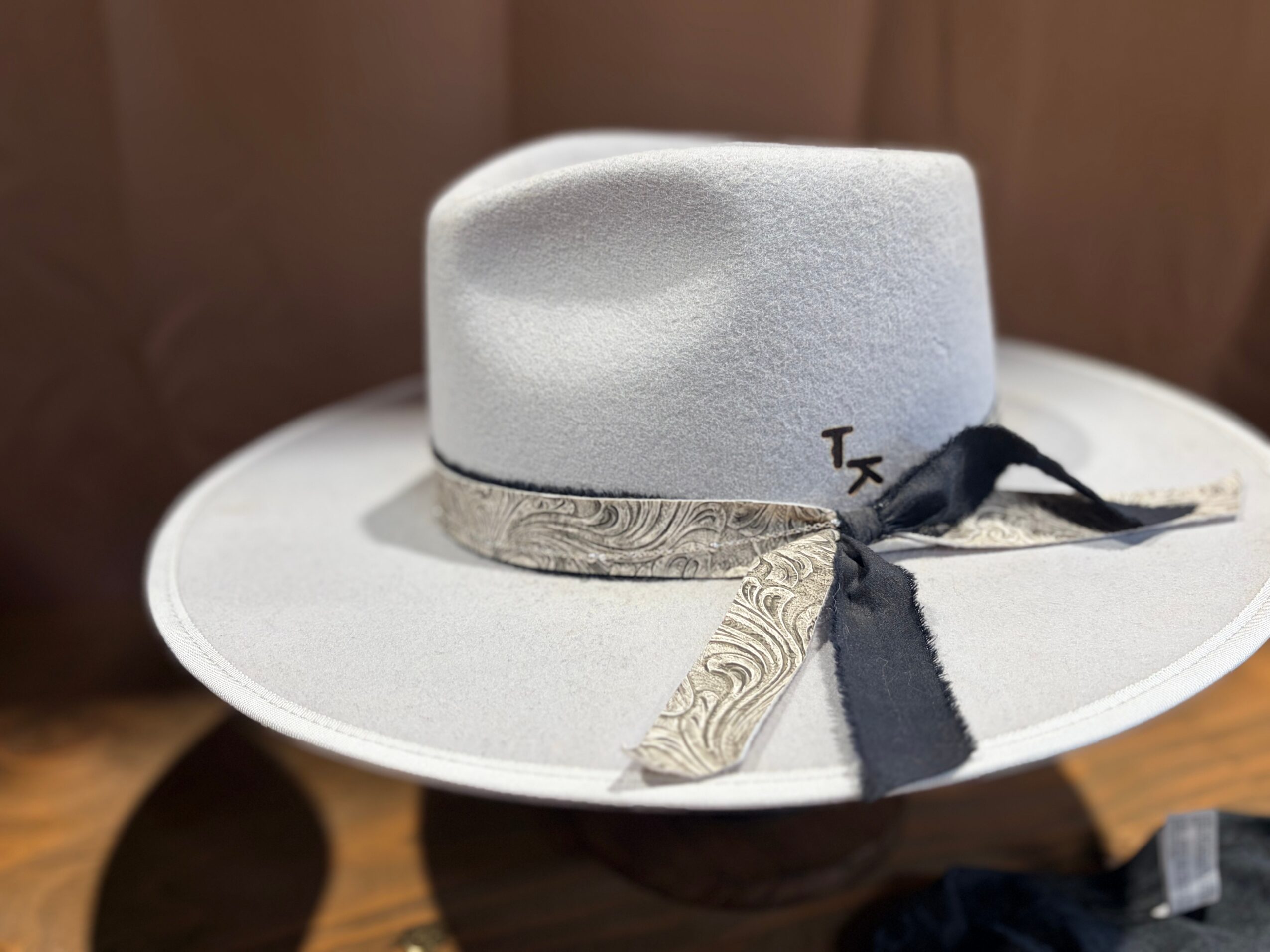 A light-colored hat with a wide brim and a decorative band, placed on a small stand. The hat has a black ribbon.